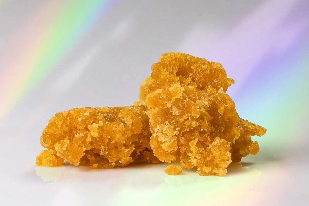 Close-up of golden cannabis wax concentrate against a soft rainbow background — shop concentrates at b\well, Provincetown's queer owned cannabis dispensary on Cape Cod.
