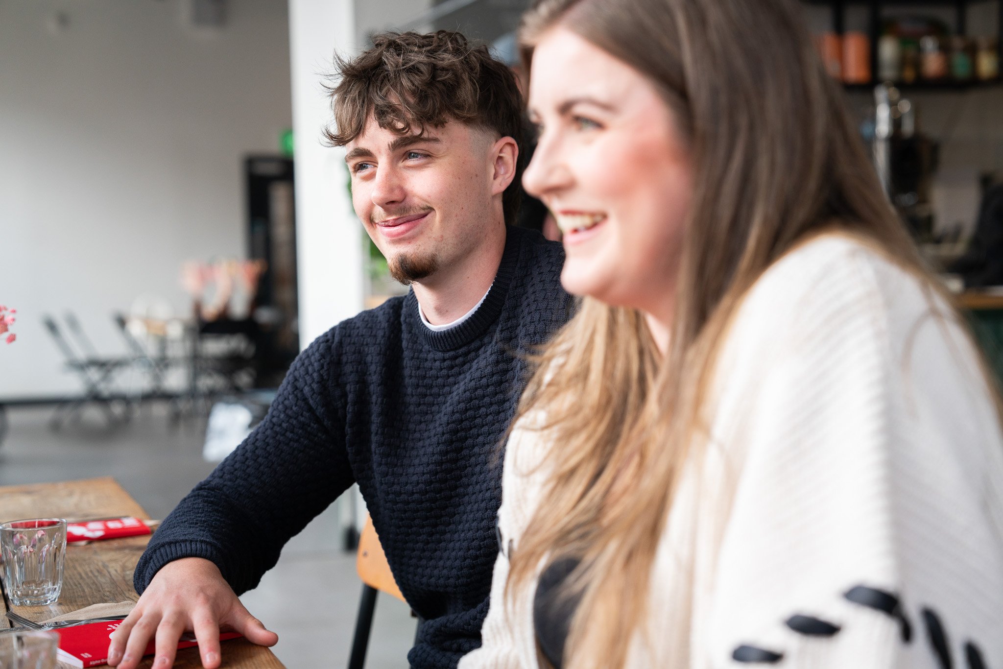 A young man and a young woman sitting at a table, smiling and enjoying each other's company in a cozy cafe setting.