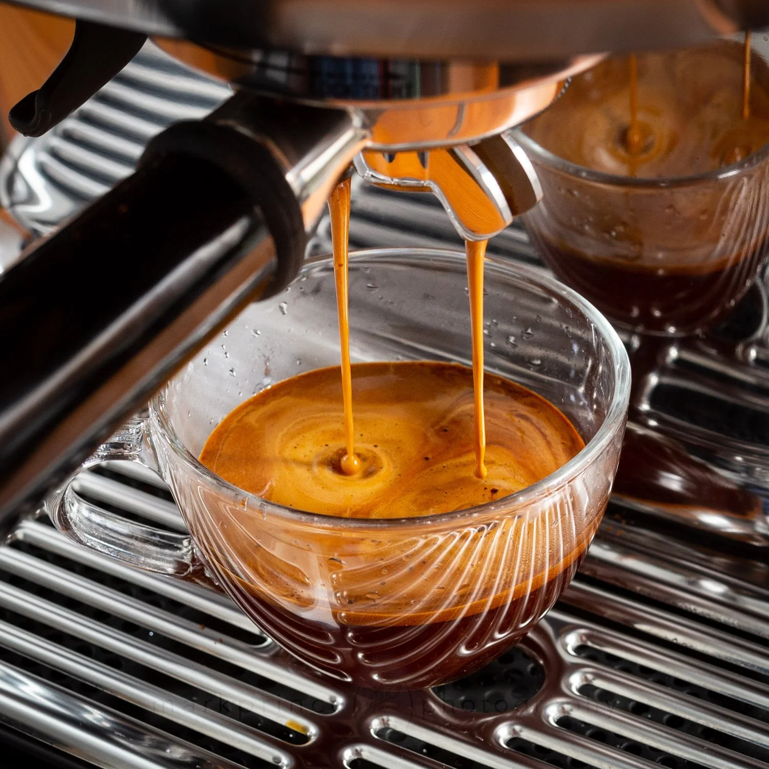 Close-up of an espresso machine pouring freshly brewed espresso into a clear glass cup, with another cup in the background.