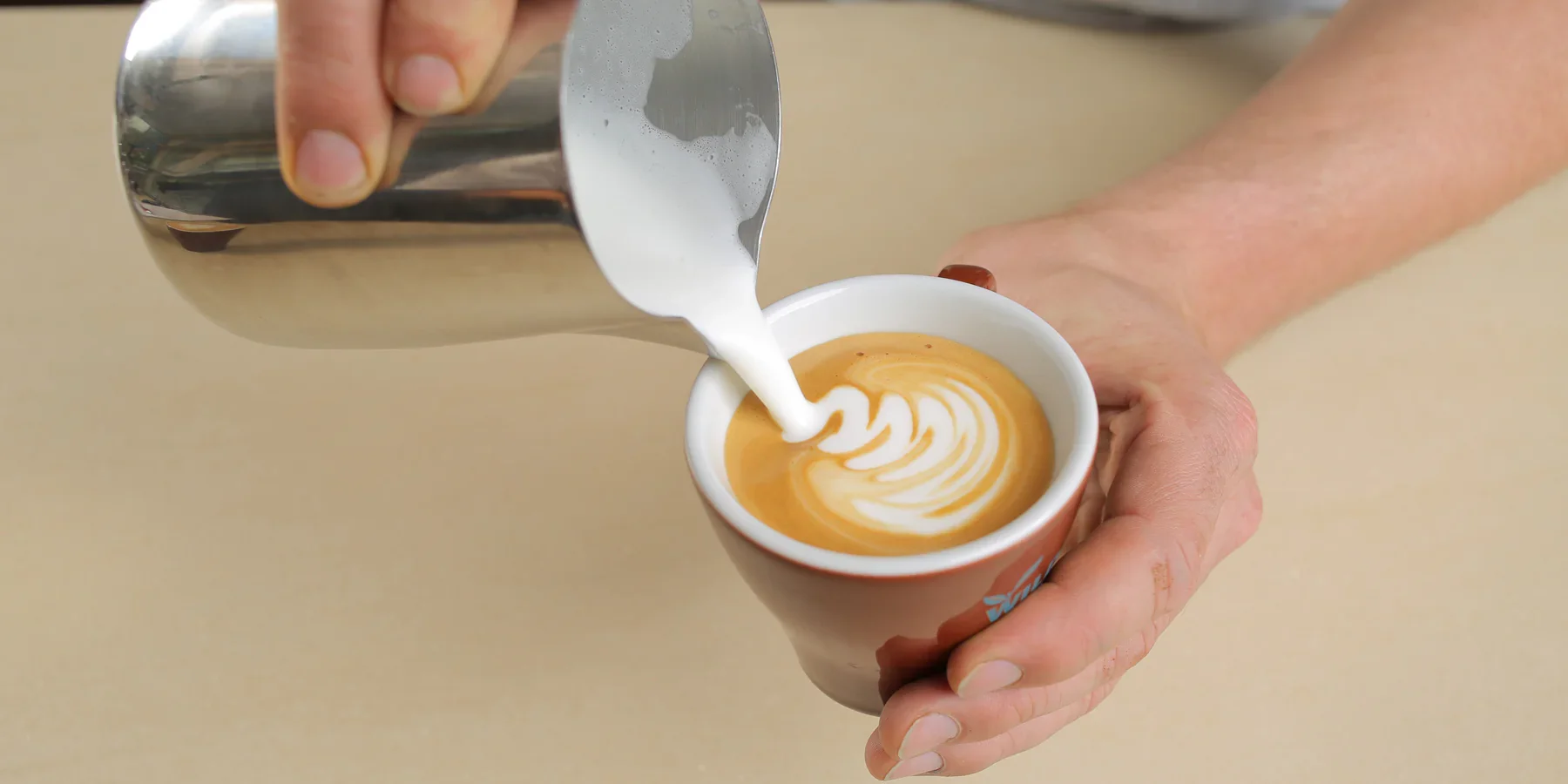 Person pours steamed milk into a cup of espresso to make latte art on top.