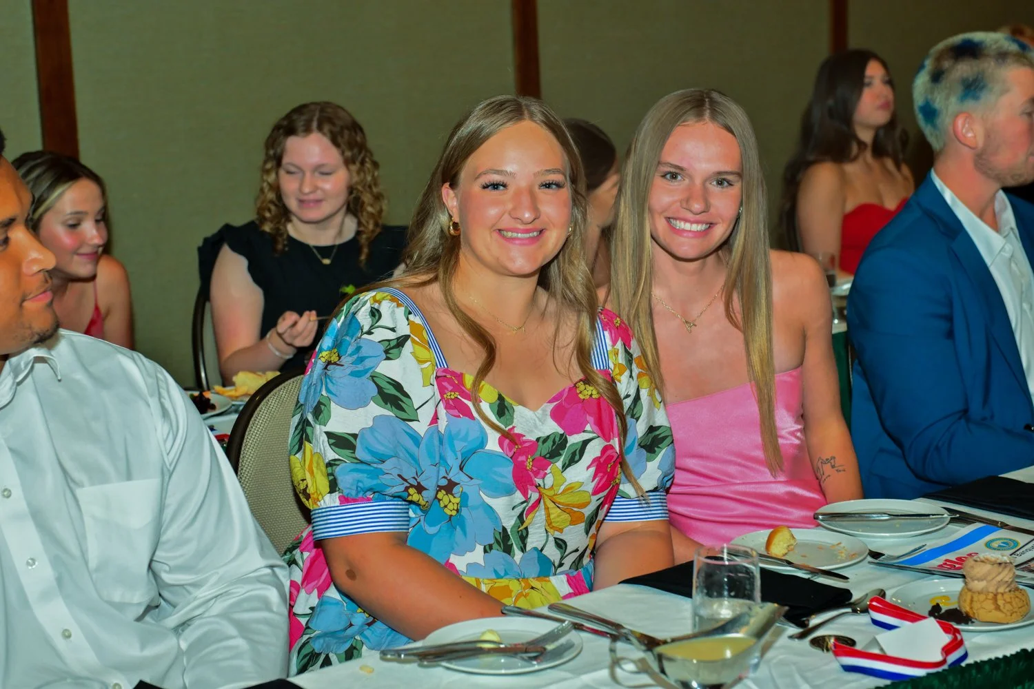 People sitting at a banquet table during a formal event, smiling and dressed in colorful clothing.