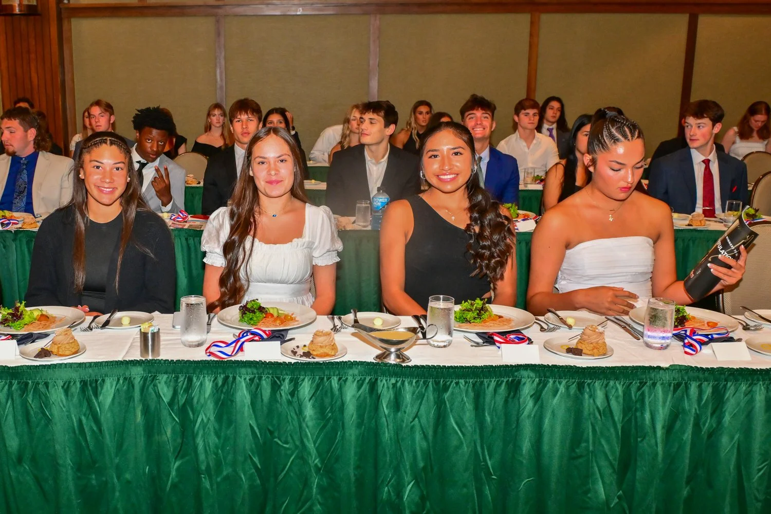 Group of well-dressed young people sitting at a formal dinner table during an event or celebration.