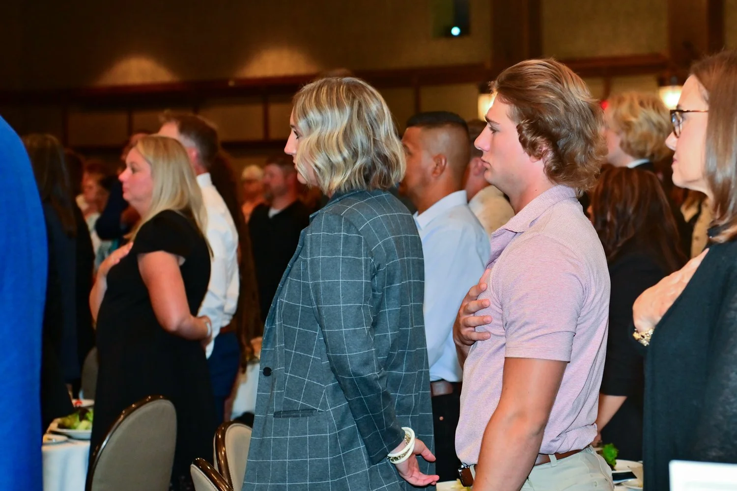 People standing during the national anthem at a formal indoor event.