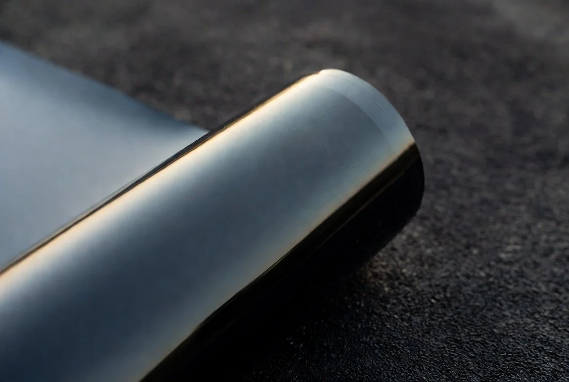 Close-up of a sleek metallic object with a curved edge resting on a textured black surface.