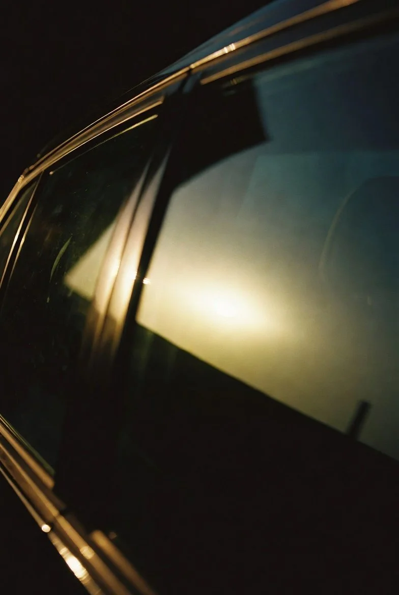 Close-up of a car's front windshield at night, with reflections and light glare visible on the glass.