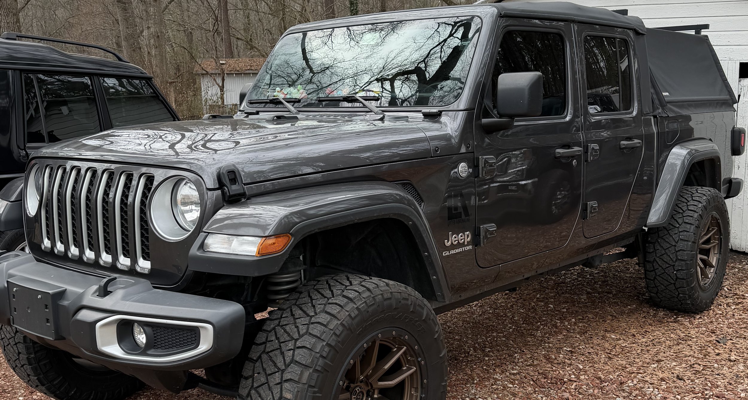 Black Jeep Gladiator with off-road tires parked on gravel.