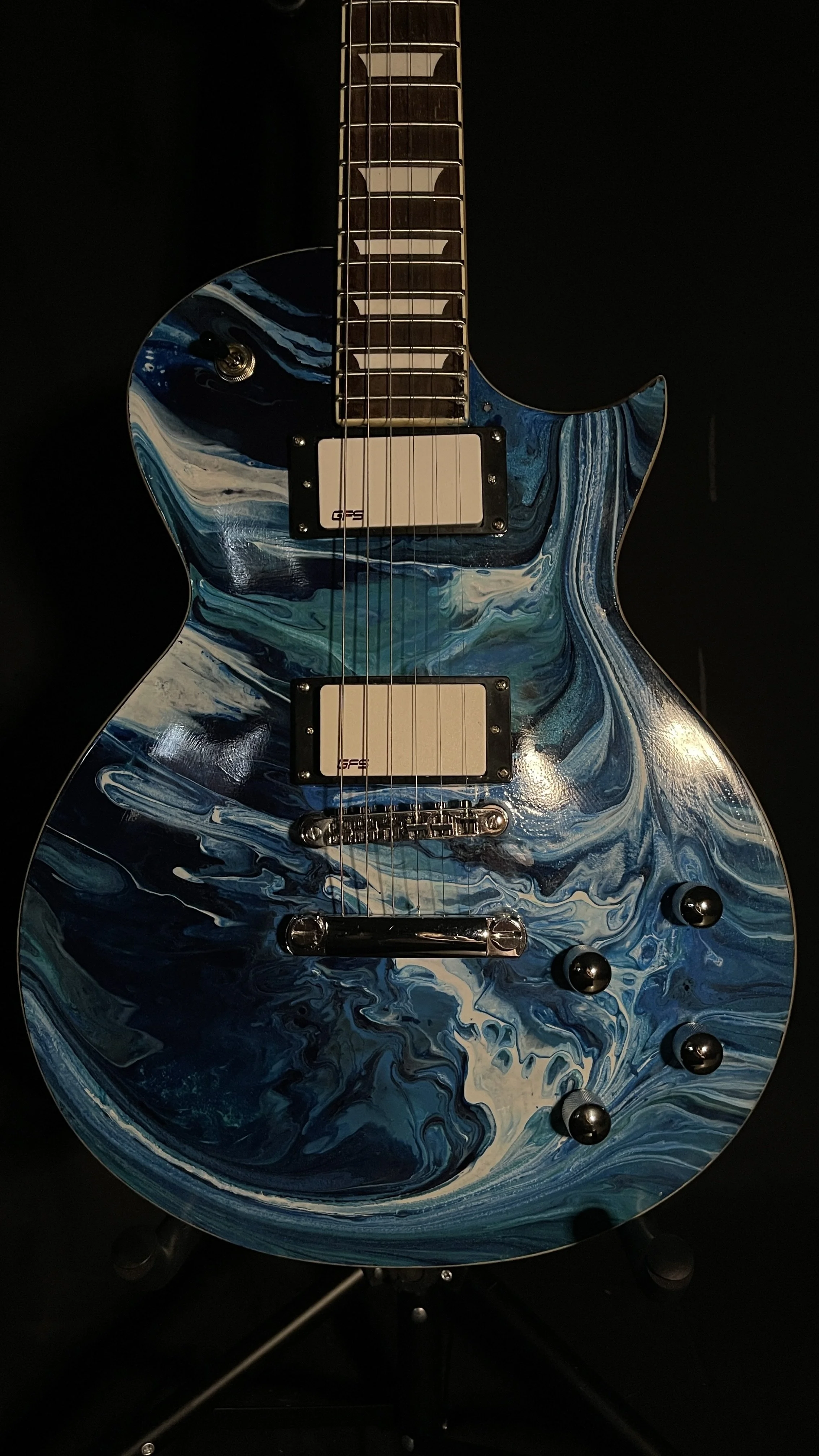 Electric guitar with a blue, white, and black marbled pattern on the body, dual humbucker pickups, black control knobs, and a dark fretboard against a black background.