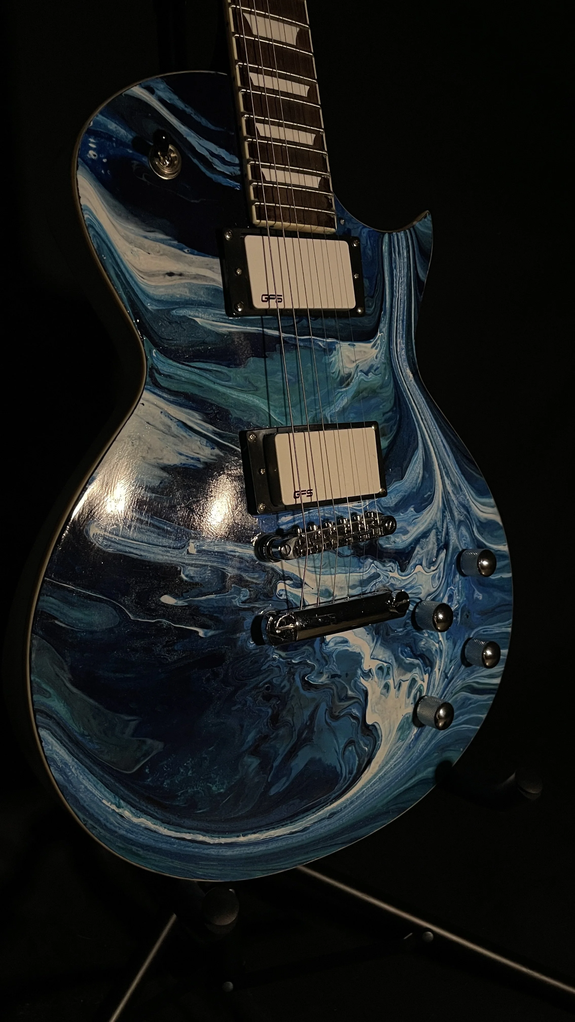An electric guitar with an acrylic pour in a wide array of blues named orpheus by Grainrot Guitars