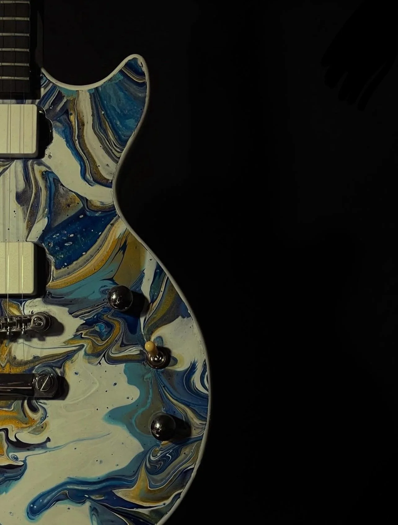 The white, gold and light blue side of an acrylic poured electric guitar named Gemini.