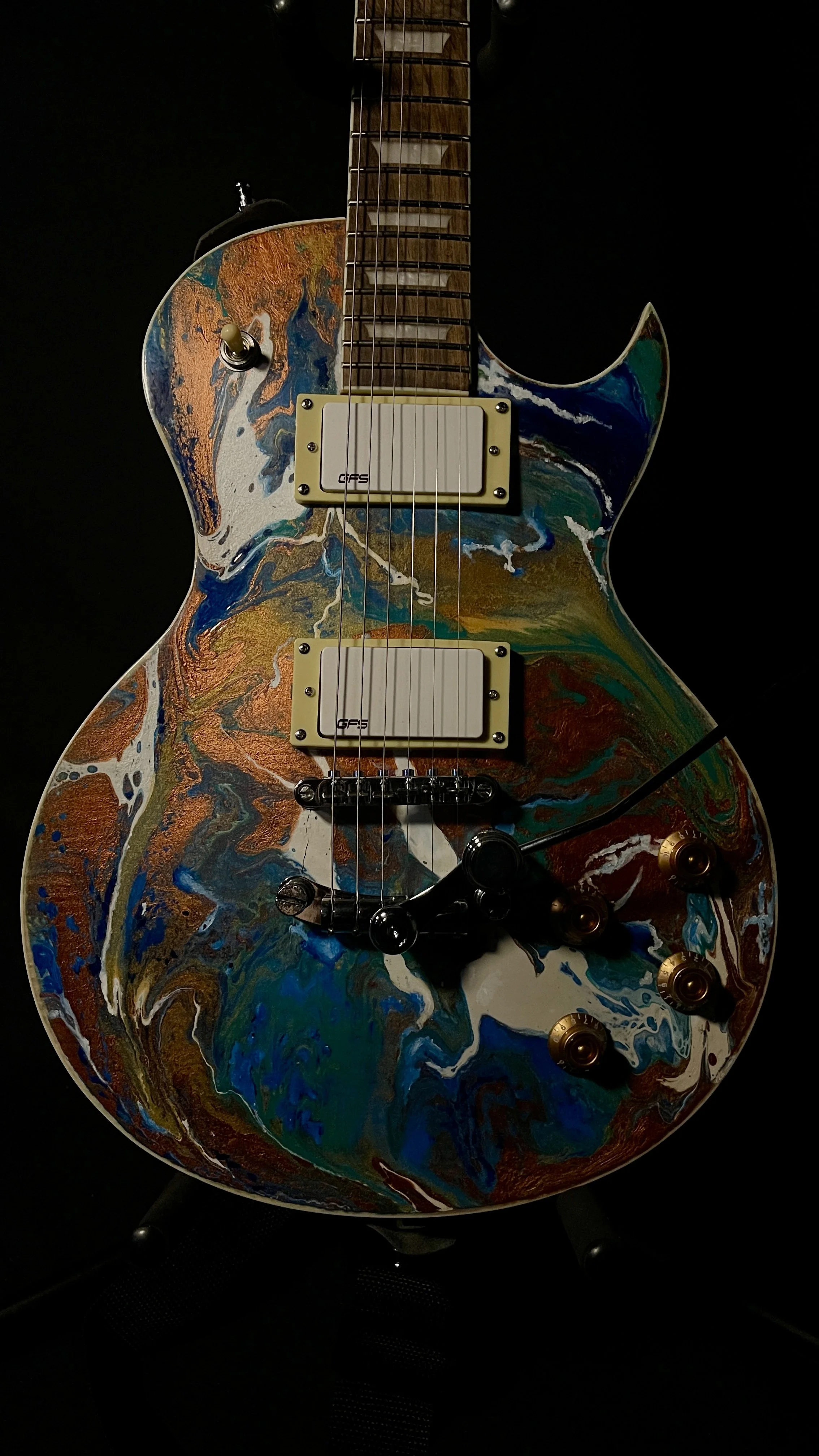 Electric guitar with a colorful, abstract swirl paint design, featuring gold control knobs and dual pickups, set against a black background.