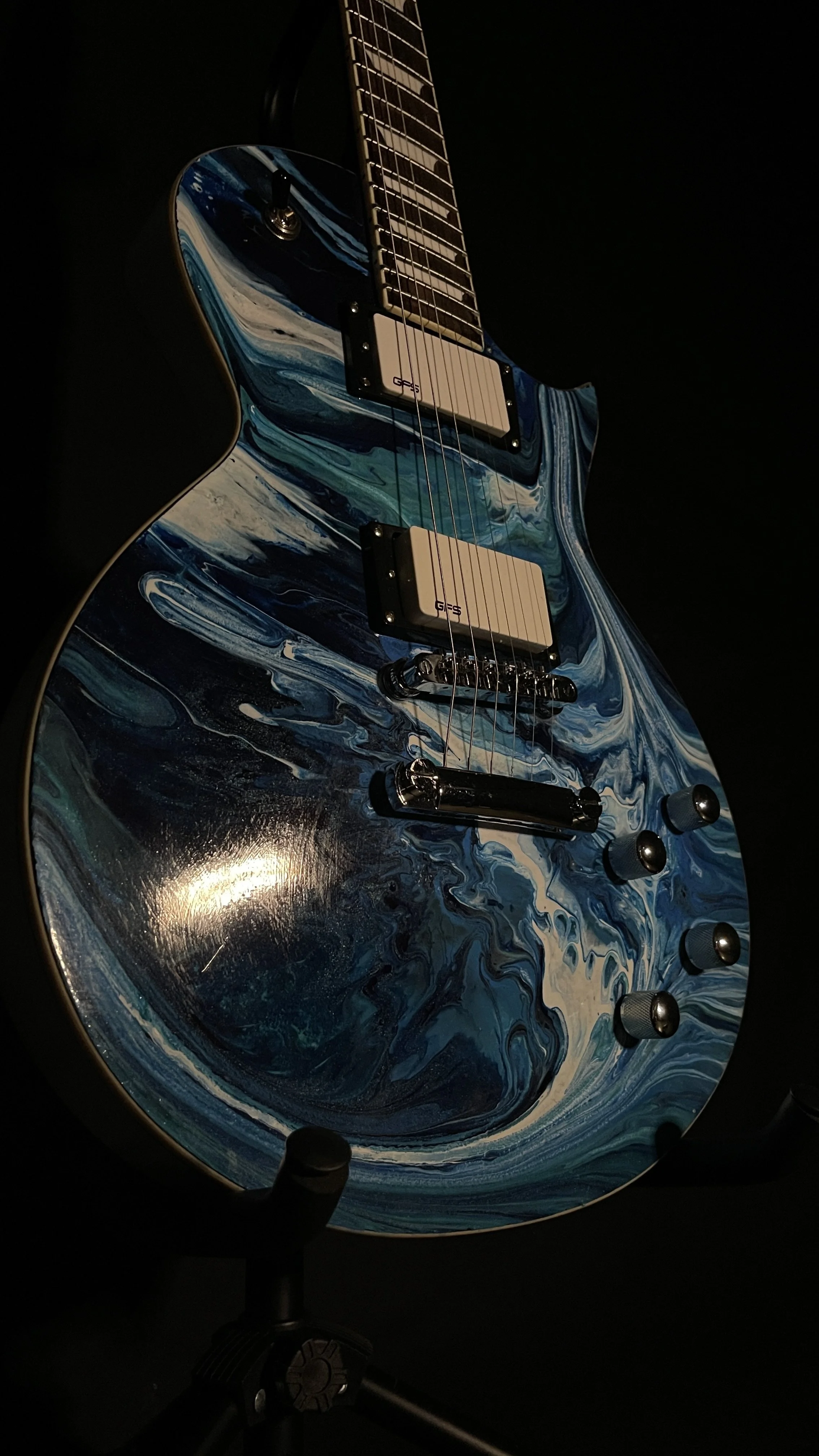 An electric guitar with an acrylic pour in a wide array of blues named orpheus by Grainrot Guitars