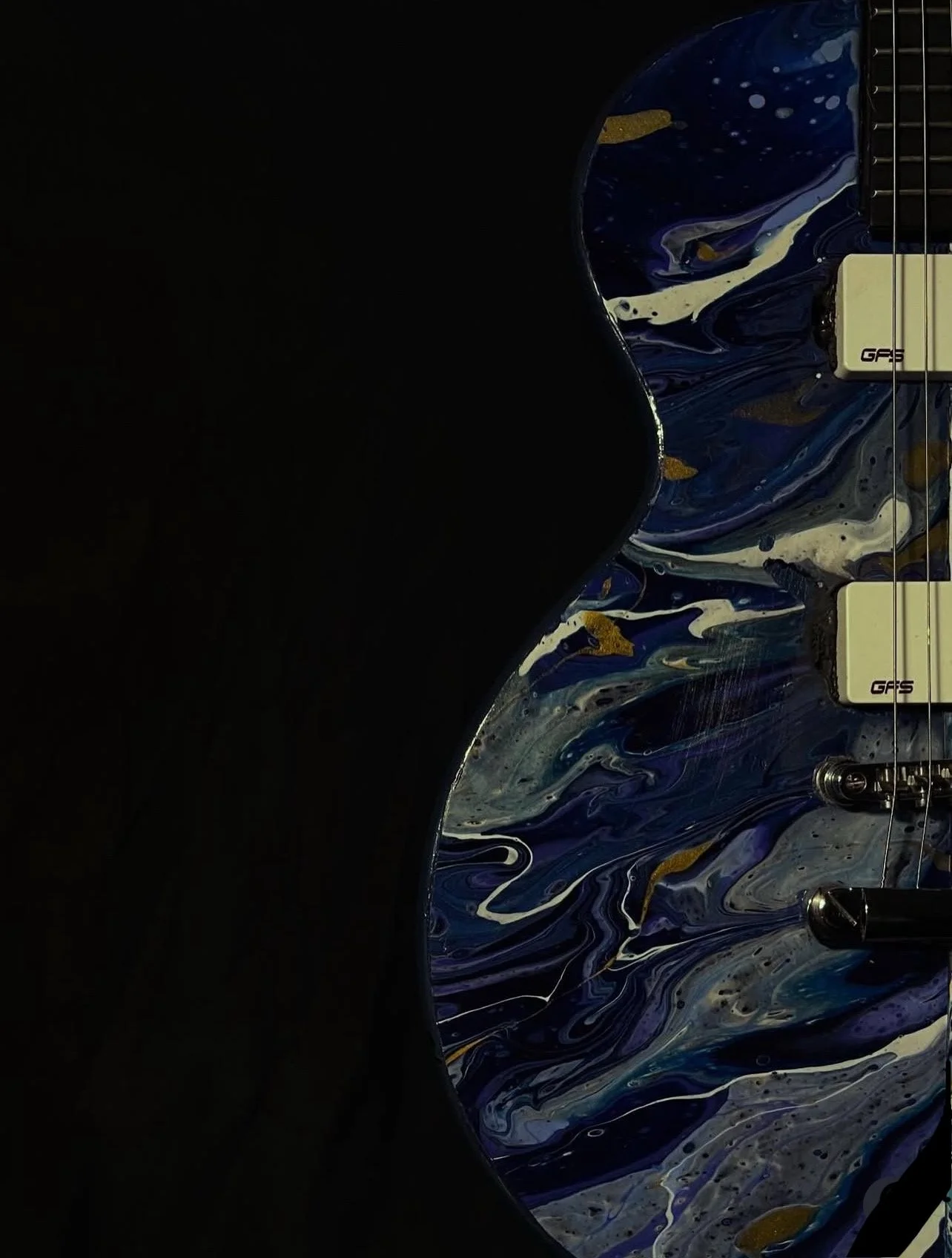 The dark blue, black and purple side of an acrylic poured electric guitar named Gemini.