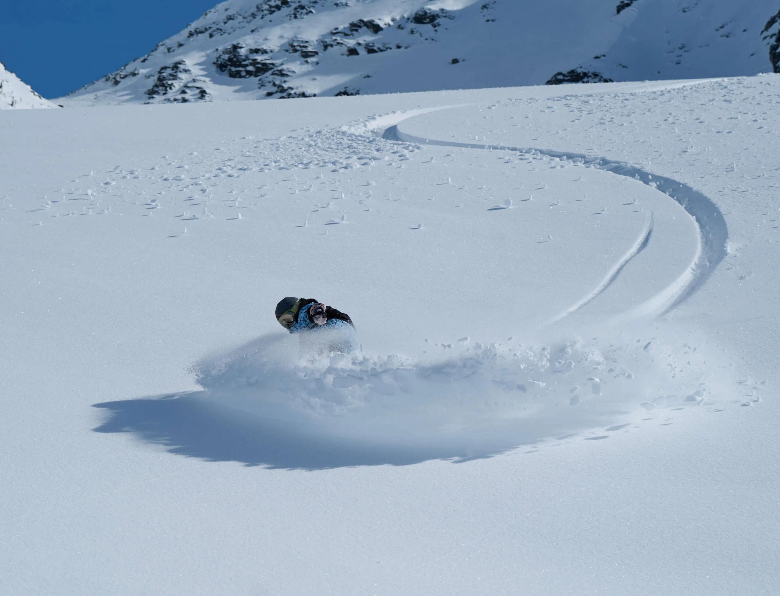 Skier making a sharp turn down a snowy mountain slope, leaving a trail of snow behind.