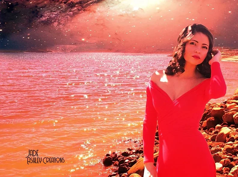 A young woman in a red dress standing on a rocky shoreline with a sparkly ocean and a glittering, colorful sky in the background.