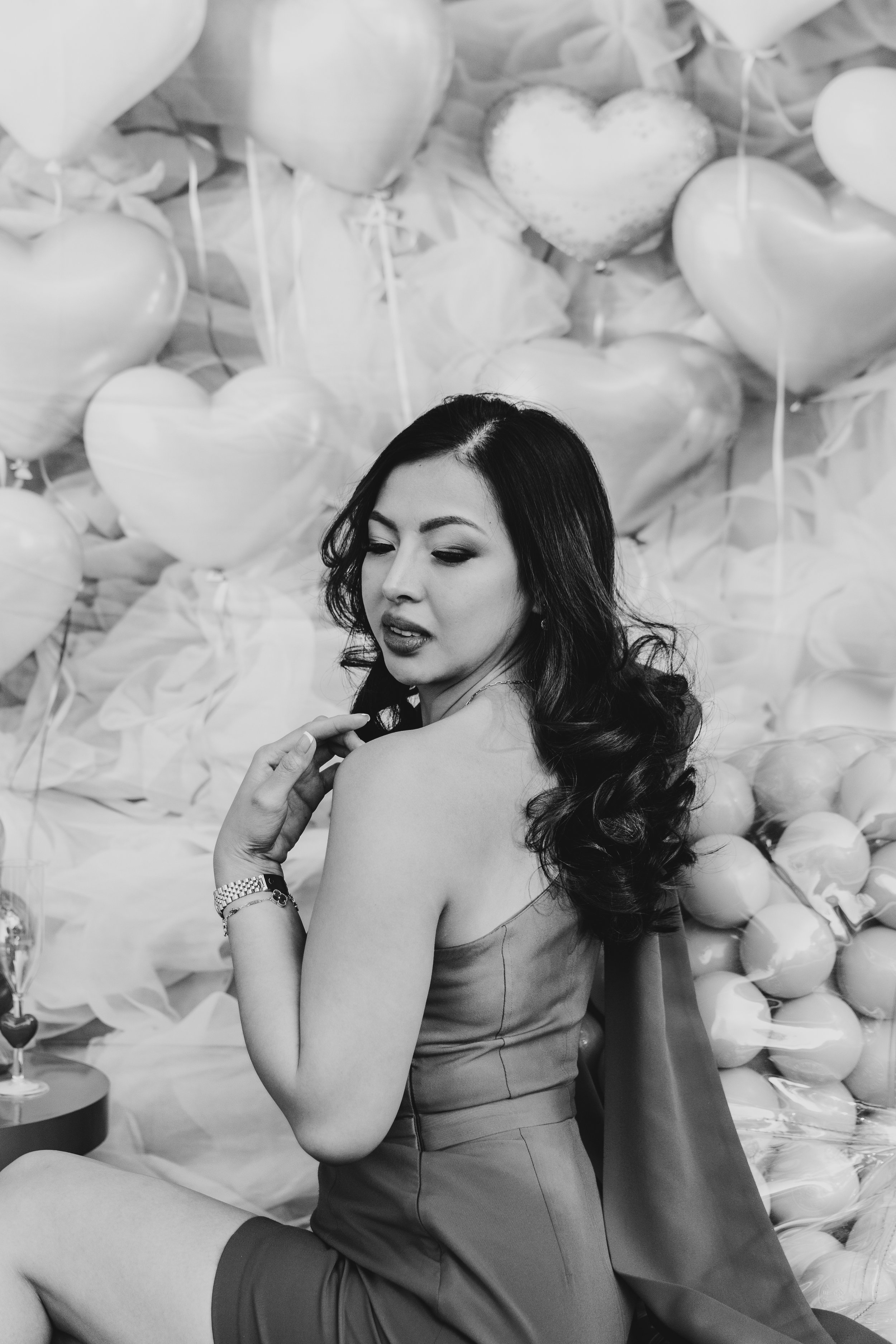 A woman with long, wavy hair looking over her shoulder, surrounded by heart-shaped balloons.