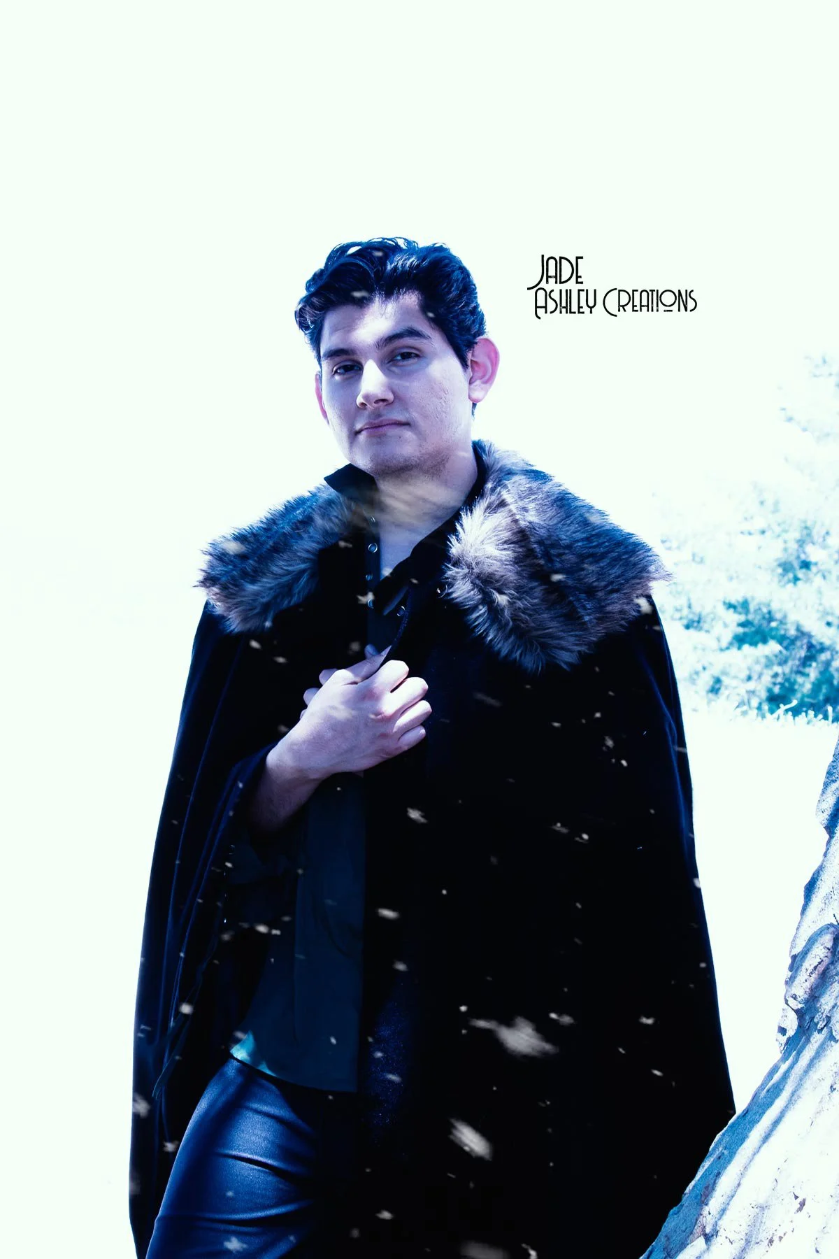 A young man in a black coat with a fur collar, standing outdoors in a snowy landscape, holding his coat with one hand, with the text 'Jade Ashley Creations' in the background.