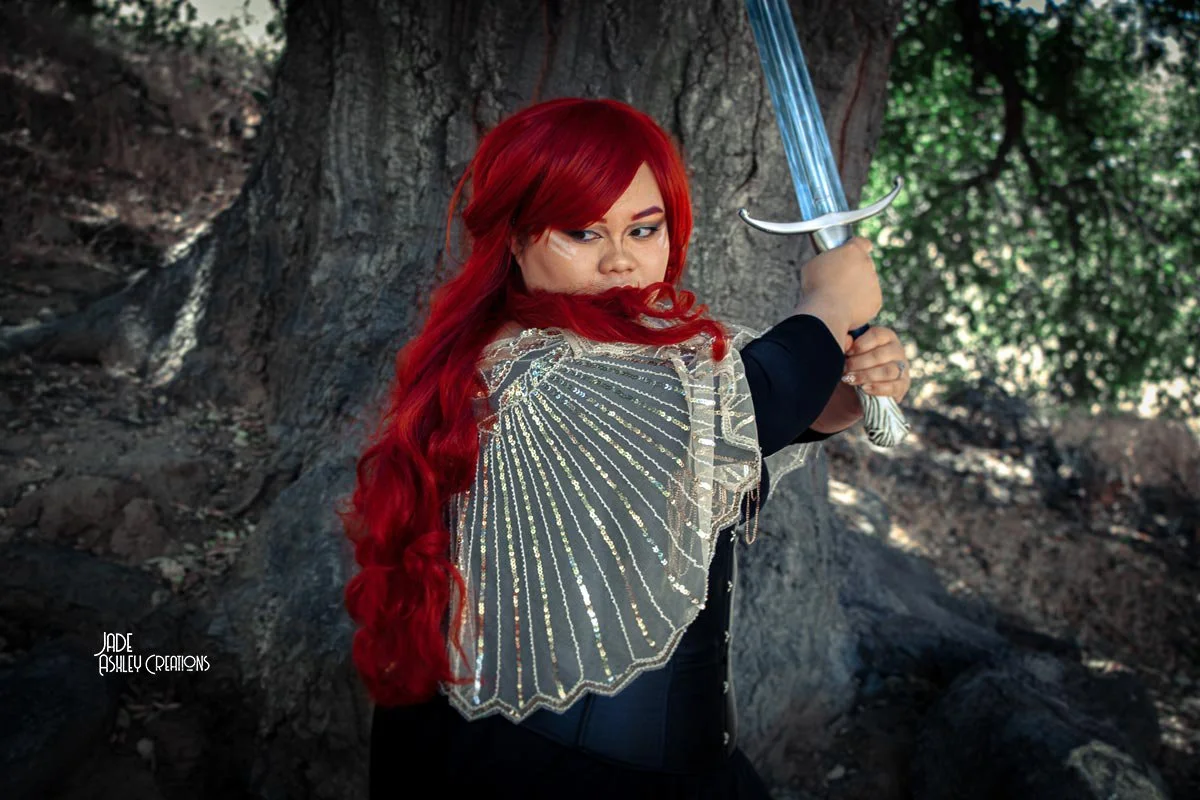 woman dressed in a dress and armor with a sword looking like a princess with red hair