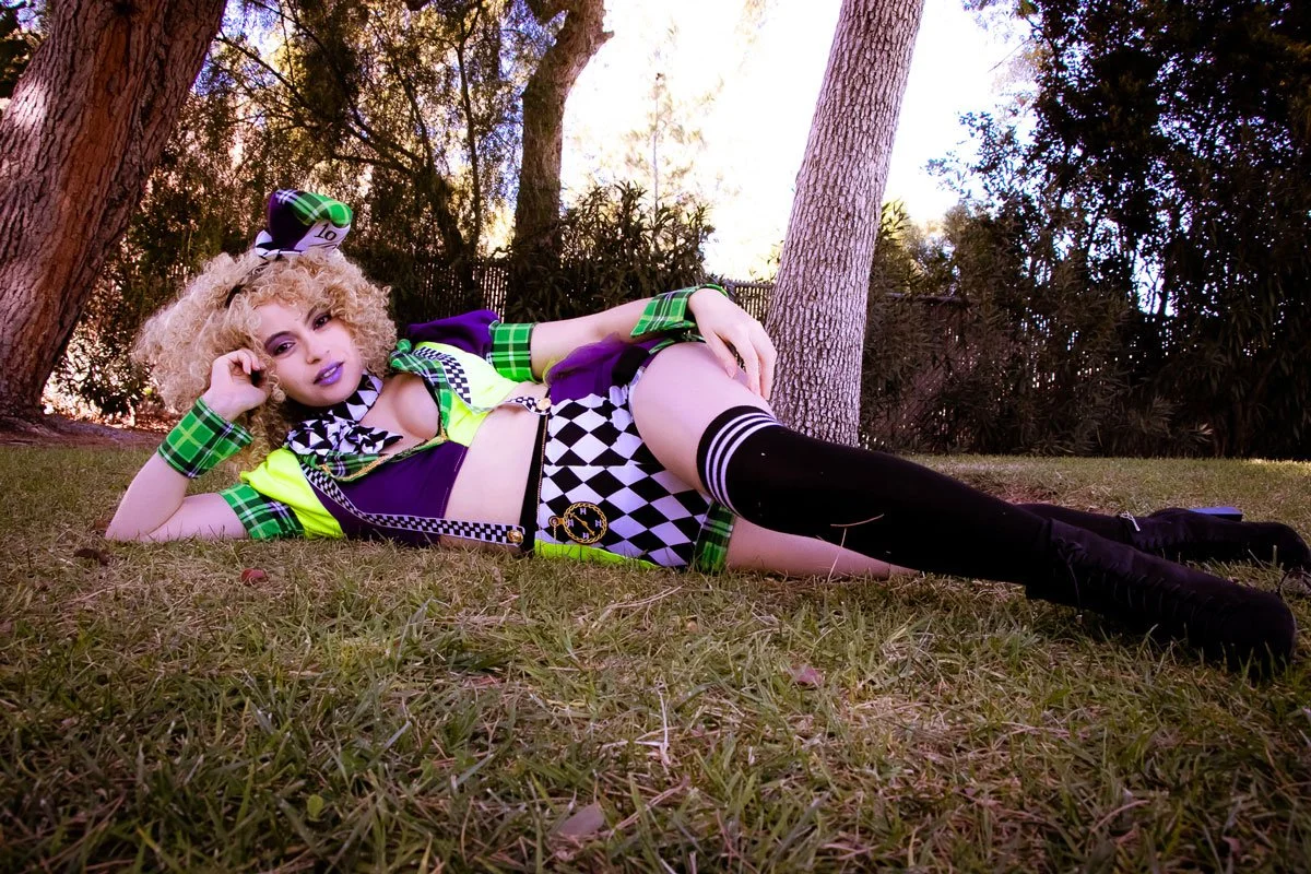 Person lying on grass outdoors in a colorful, patterned outfit with thigh-high socks, surrounded by trees.