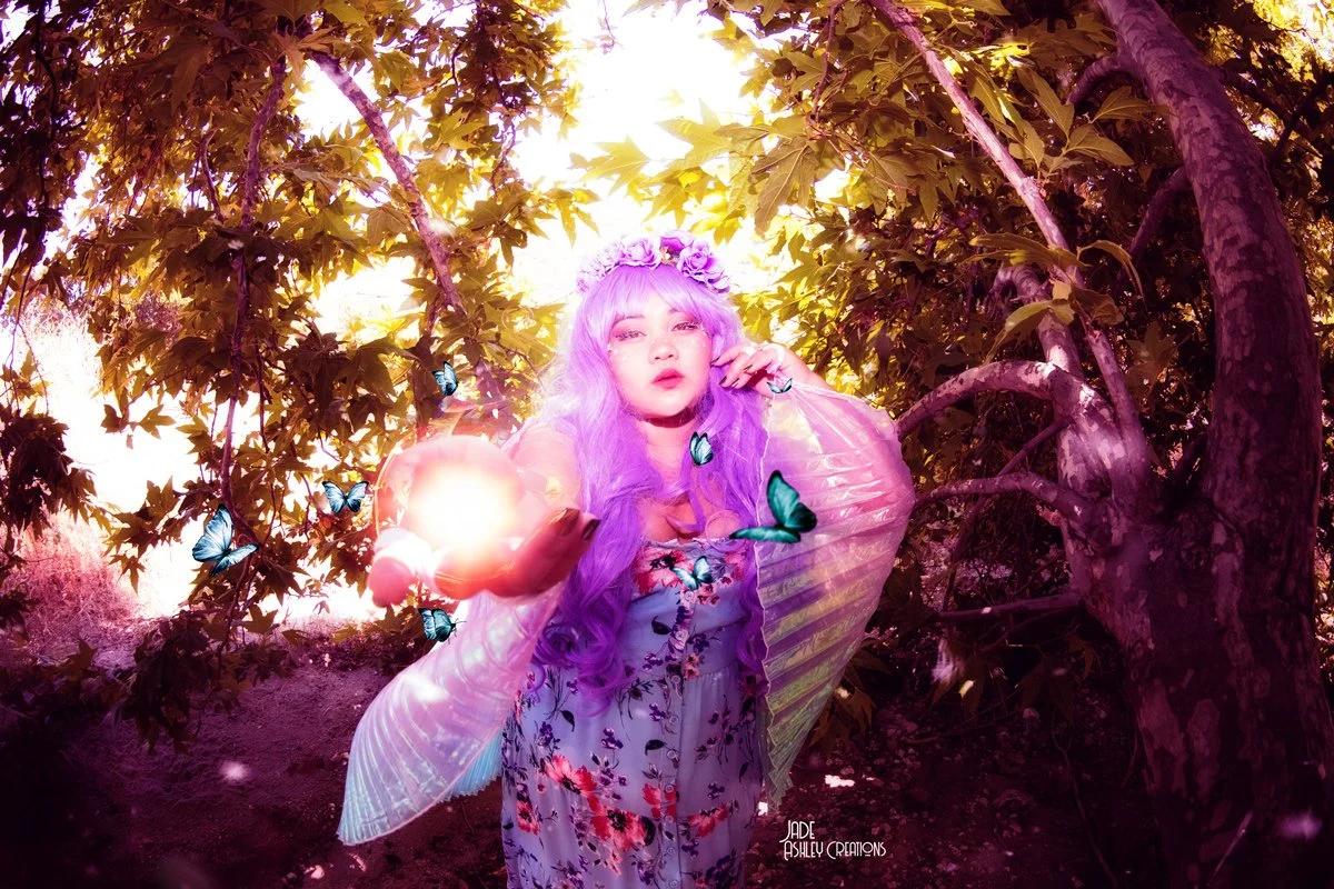 A woman with purple hair and a flower crown standing amidst trees, surrounded by blue butterflies, with sunlight filtering through the branches.