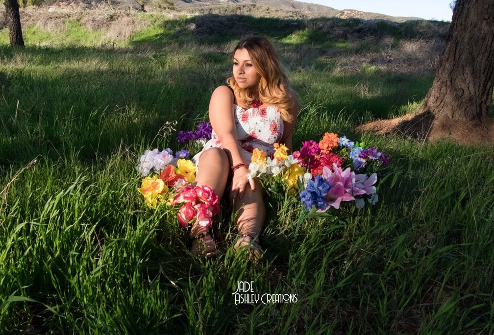 woman posing sitting down on grass with flowers around her