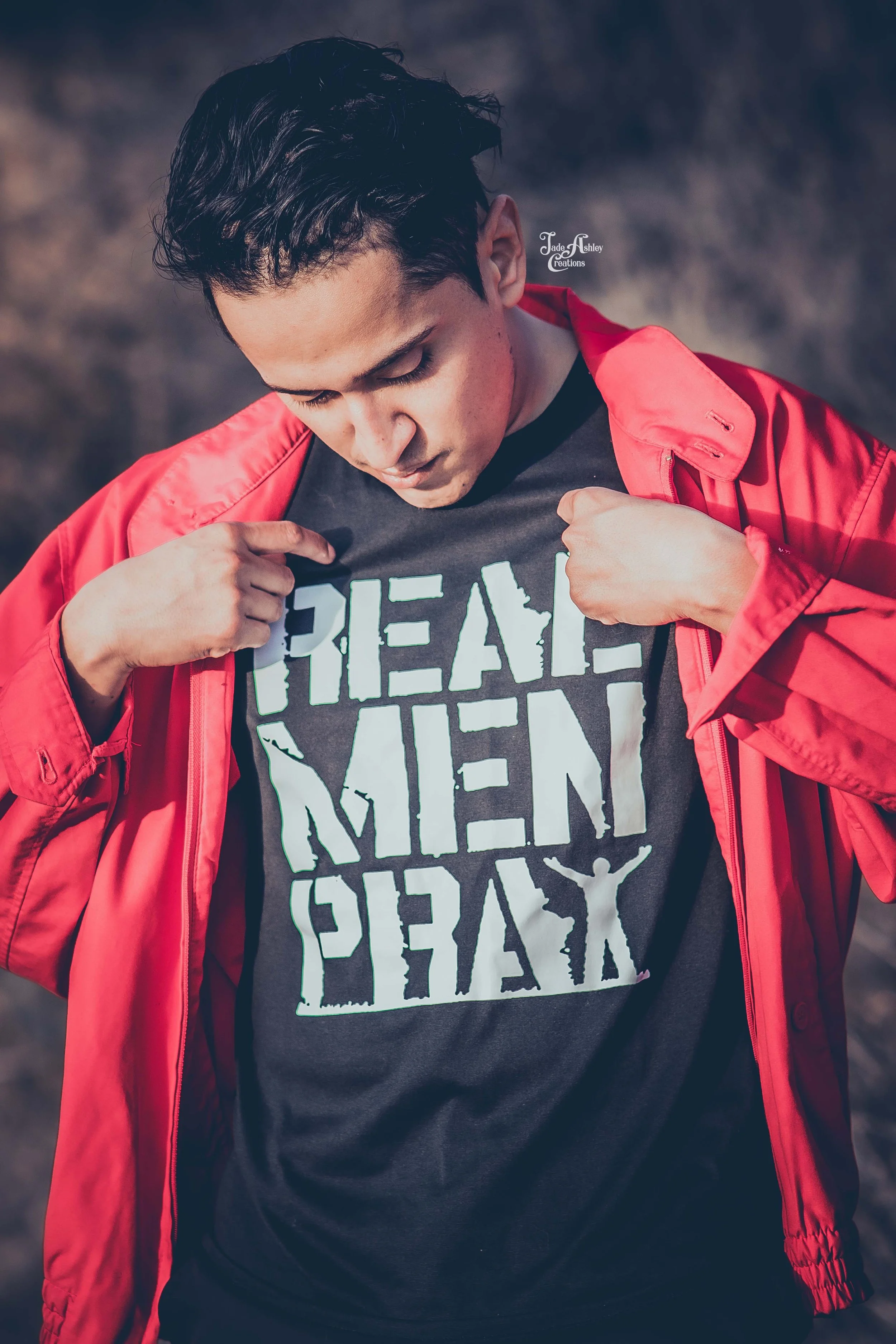 Young man wearing a red jacket showing a shirt with the text 'REAL MEN PRAY'