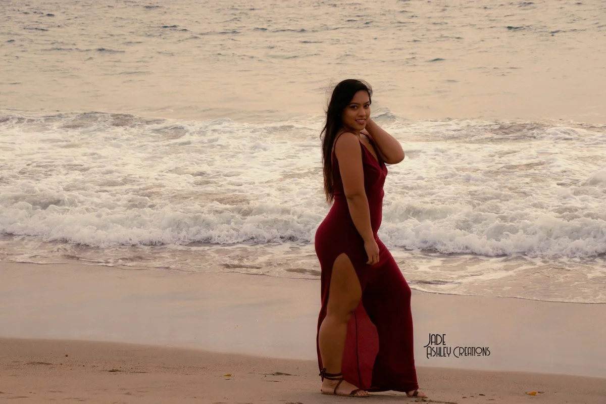 Woman in a red dress standing on the beach near the water at sunset