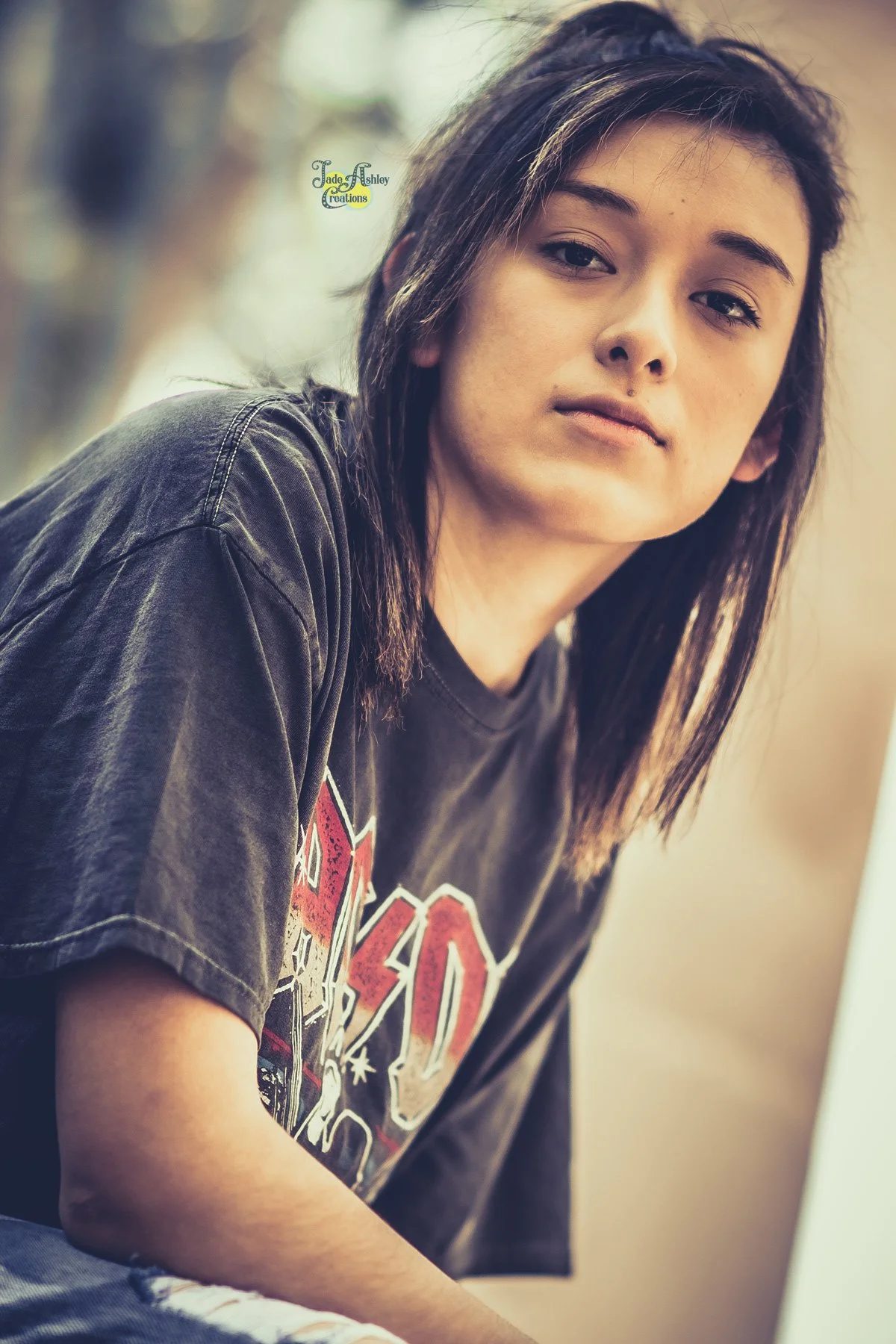 A young woman with medium-length dark hair, wearing a black graphic T-shirt and sitting indoors, looking at the camera with a neutral expression.