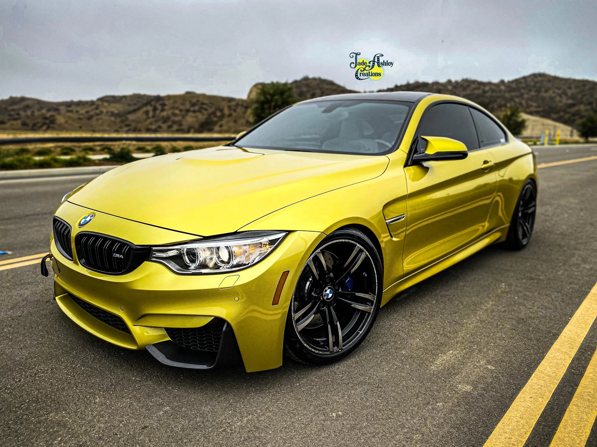 A yellow BMW sports car parked on the side of a road with mountains in the background.