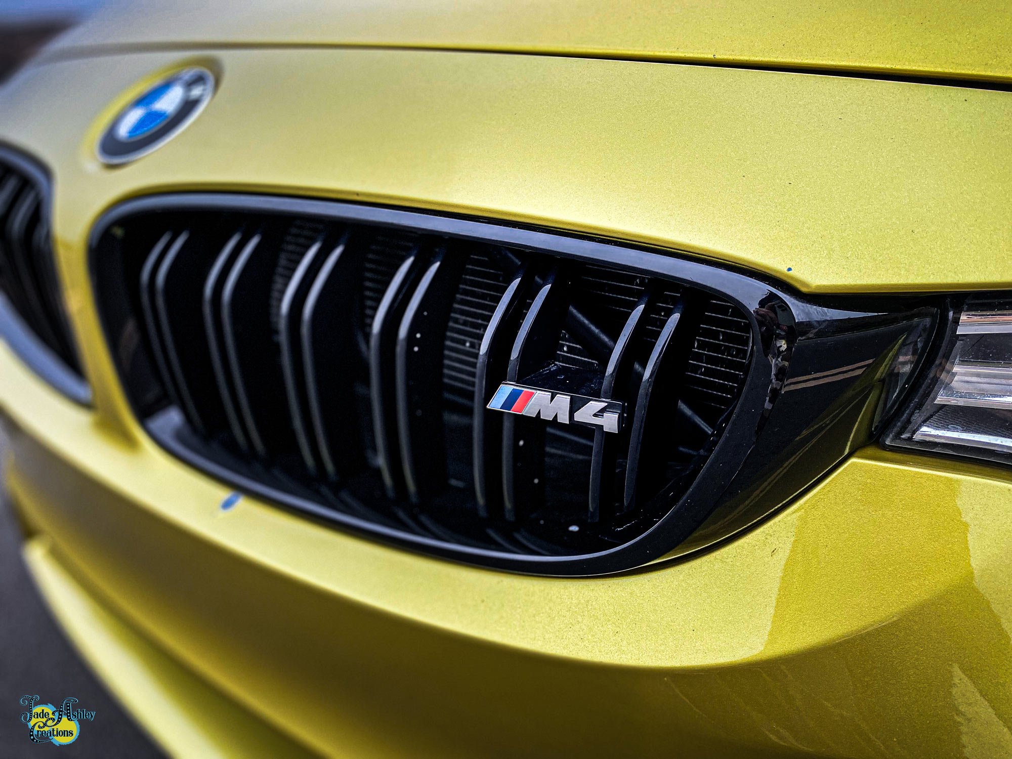 Close-up of yellow BMW car front grille with M4 badge.