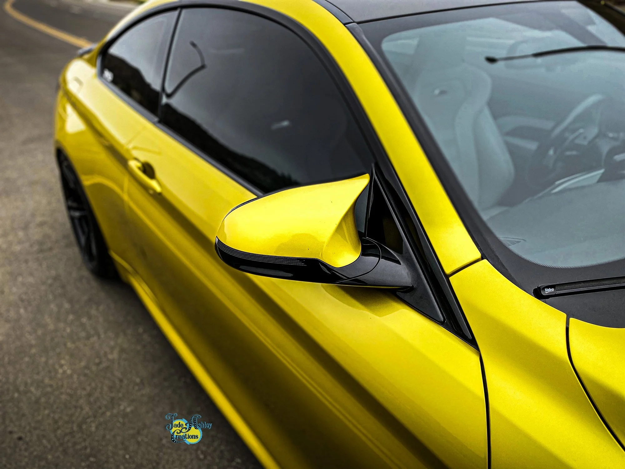 Close-up of a bright yellow sports car with black accents, including the side mirror and window trims, parked on a street.
