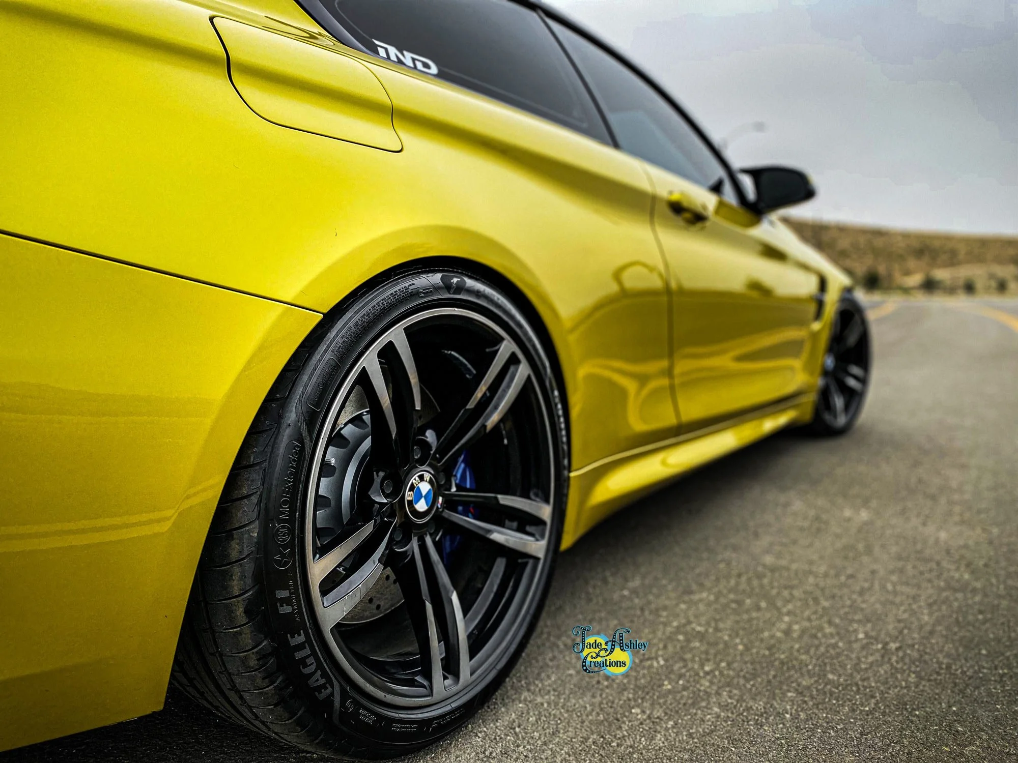 A yellow BMW sports car with black rims and blue brake calipers parked on an empty road with a cloudy sky.