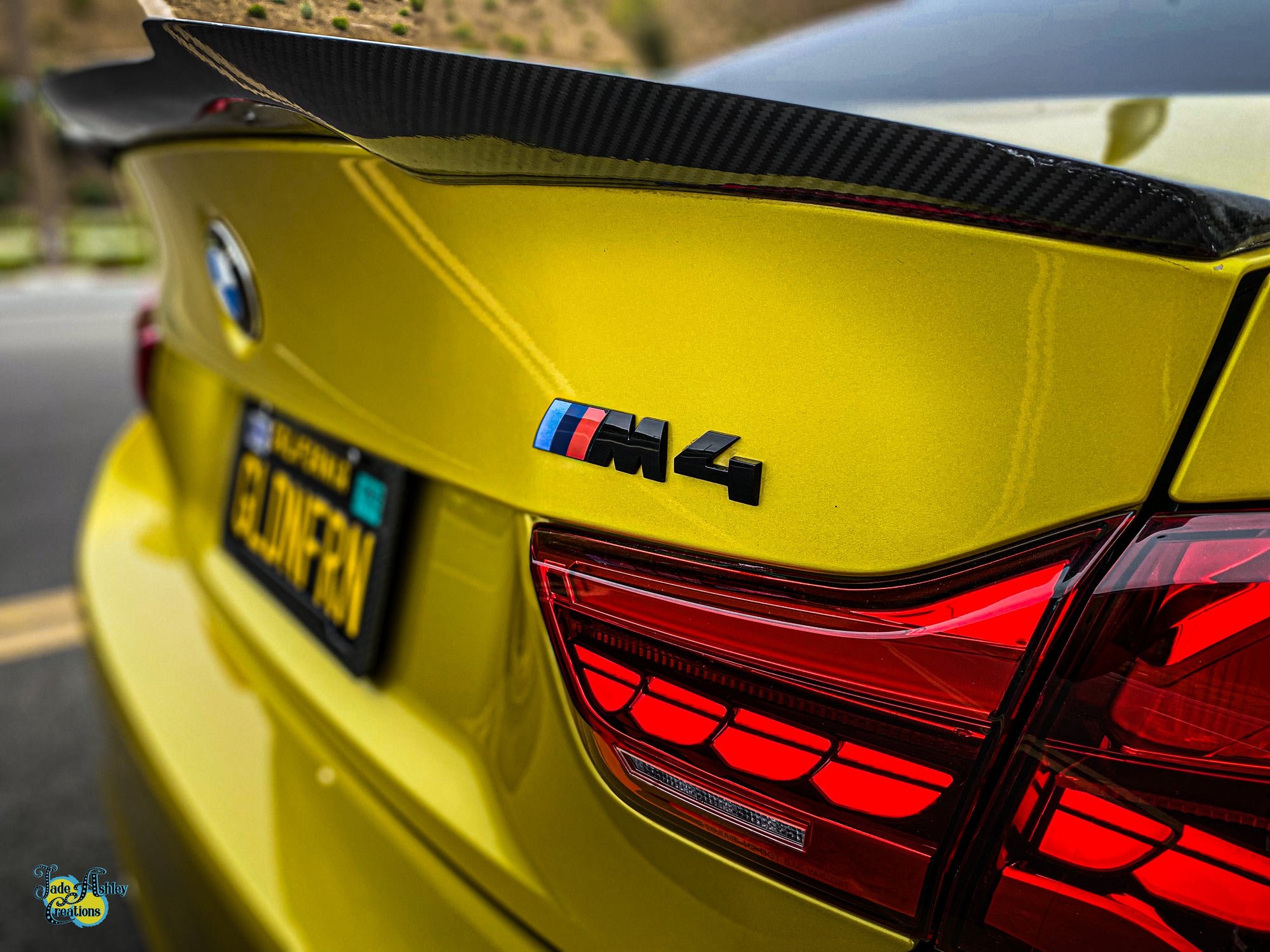 Close-up of the rear of a yellow BMW M4 car showing the M4 badge and rear taillights.