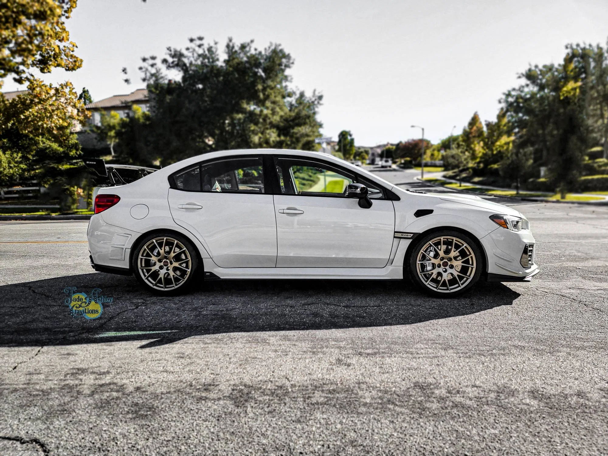 A white sports sedan car parked on a street with trees and houses in the background.