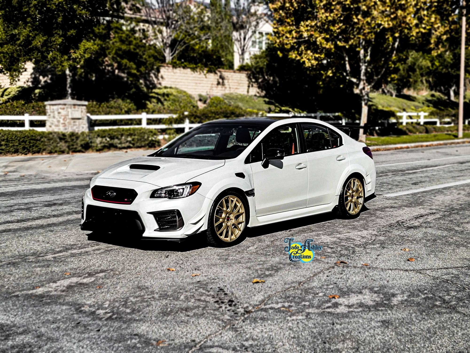 White rally car with gold wheels parked on a street with trees and a brick wall in the background.