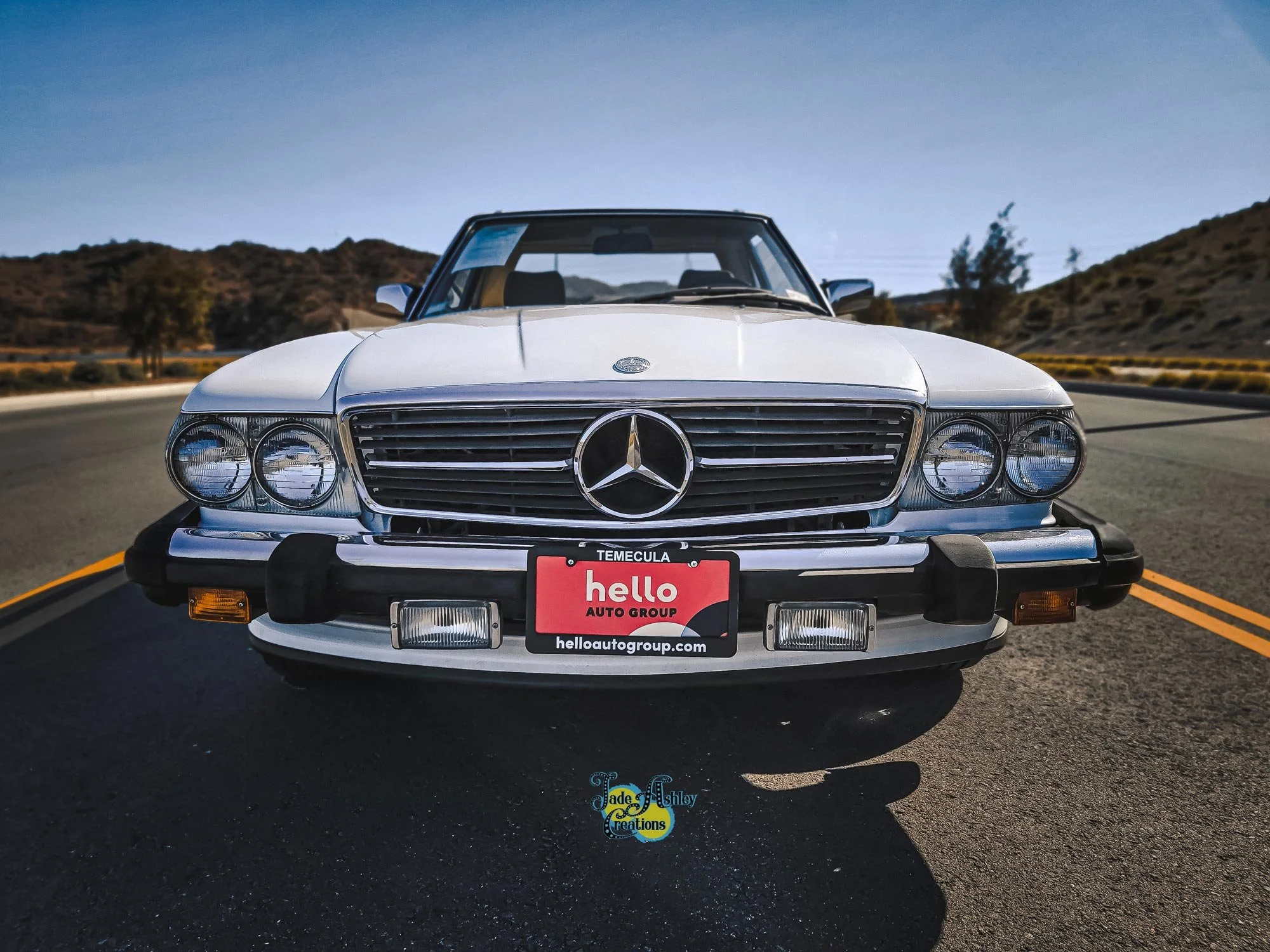 Front view of a classic white Mercedes-Benz car parked on a road with hills and a clear sky in the background.