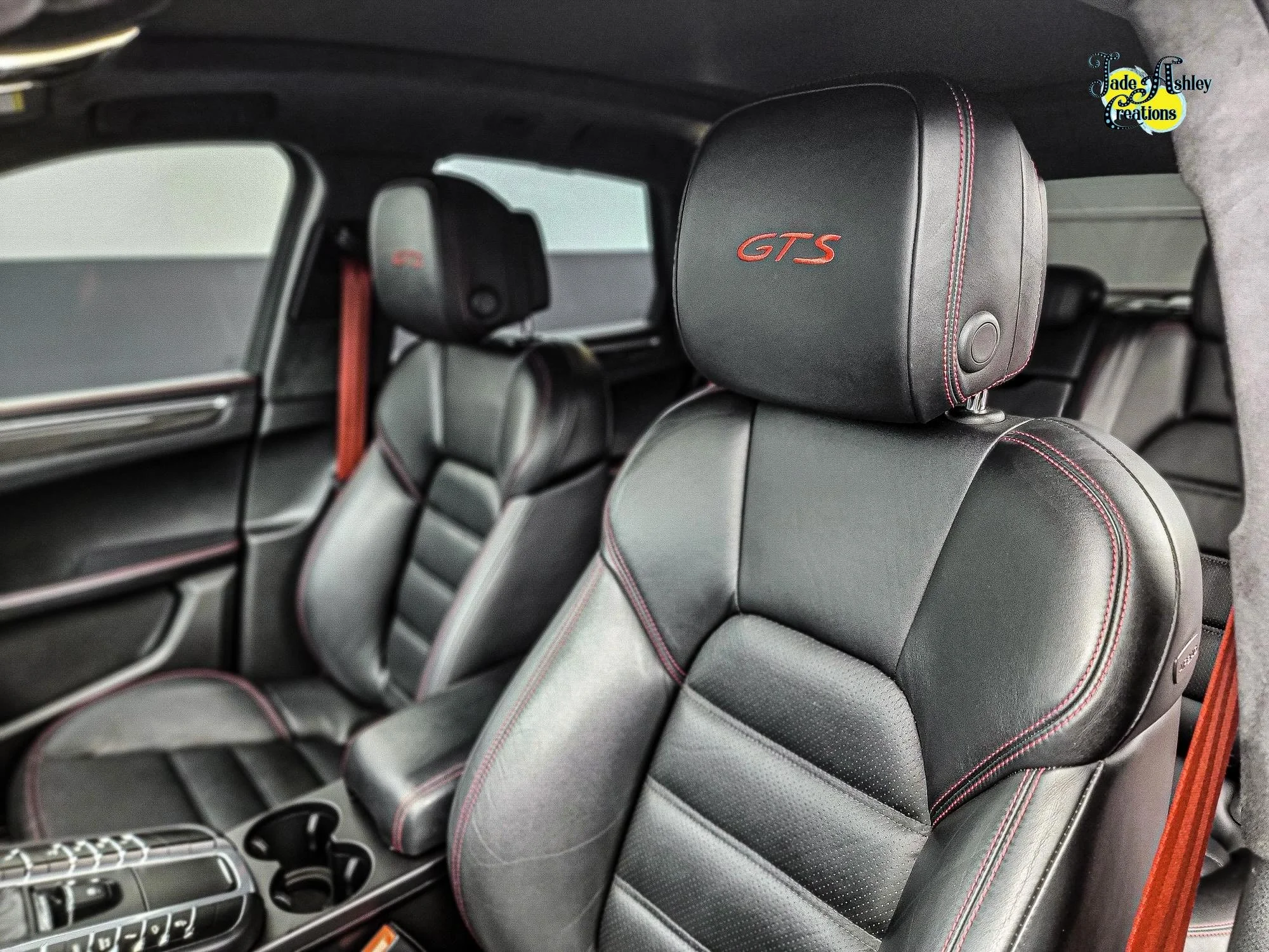 Close-up of black leather car seats with red stitching, headrest embroidered with 'GTS', inside a modern vehicle.
