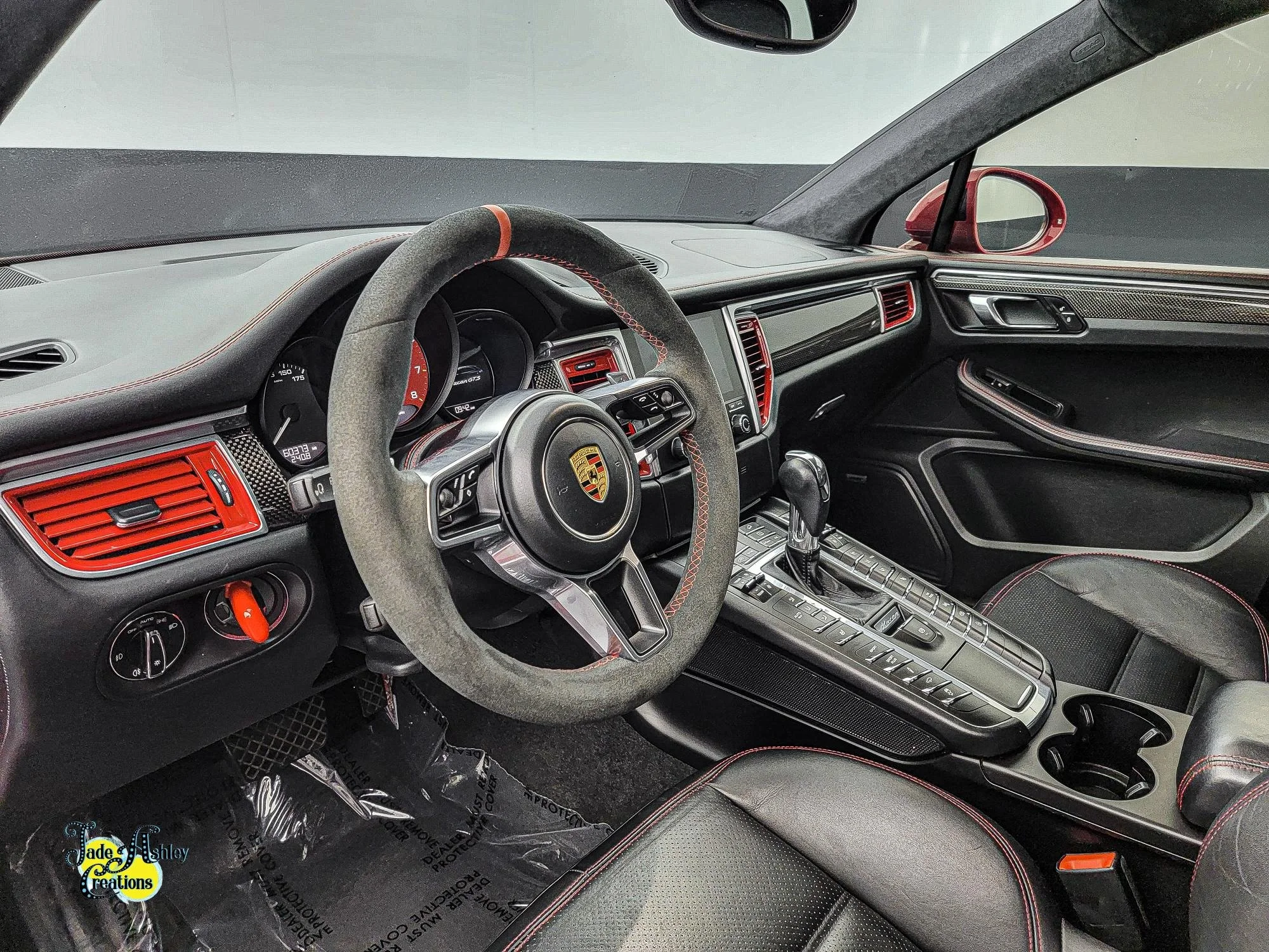 Interior of a Porsche sports car featuring a black dashboard with red accents, gray steering wheel with Porsche emblem, gear shifter, and black leather seats with red stitching.