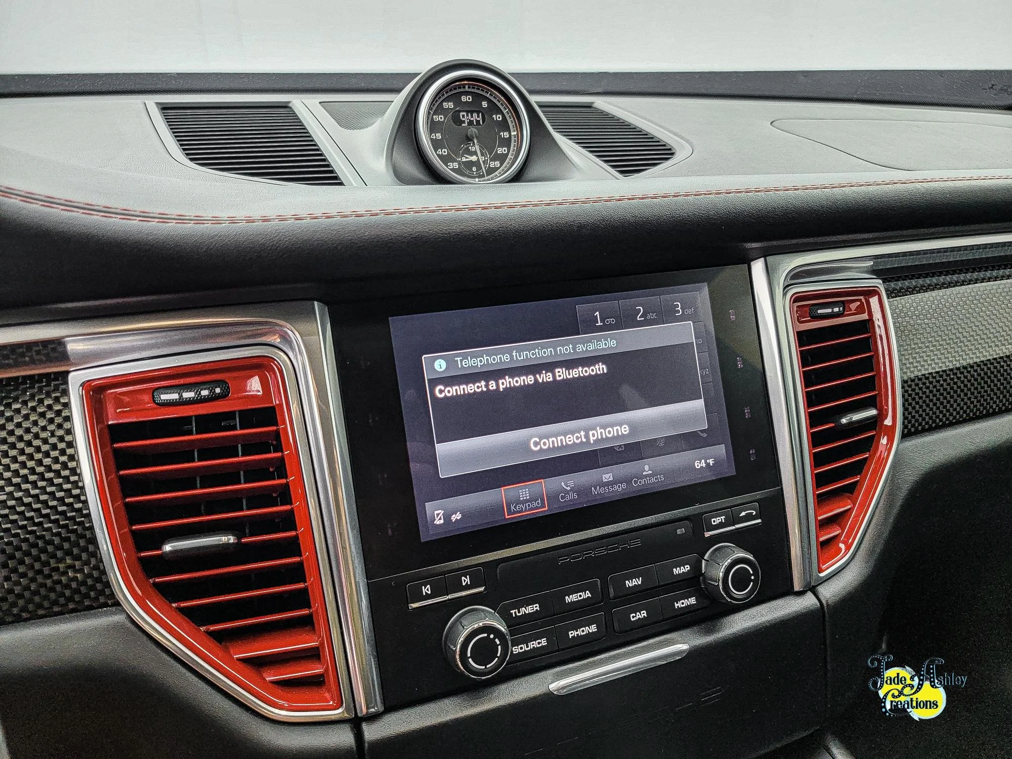 The image shows the dashboard of a car with a digital infotainment system displaying a message to connect a phone via Bluetooth, along with red accents on the air vents and a small analog clock on top of the dashboard.