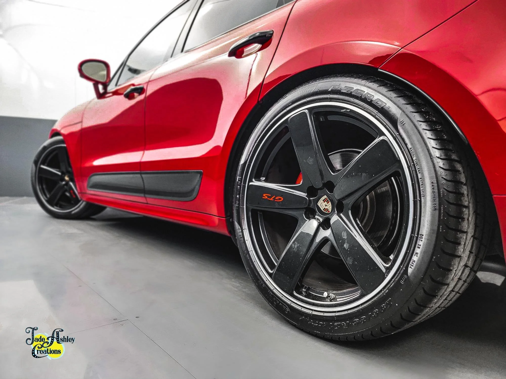 Close-up of a red Porsche car, focusing on the front wheel which features a black rim with the Porsche emblem and GTS branding, and P Zero tire.