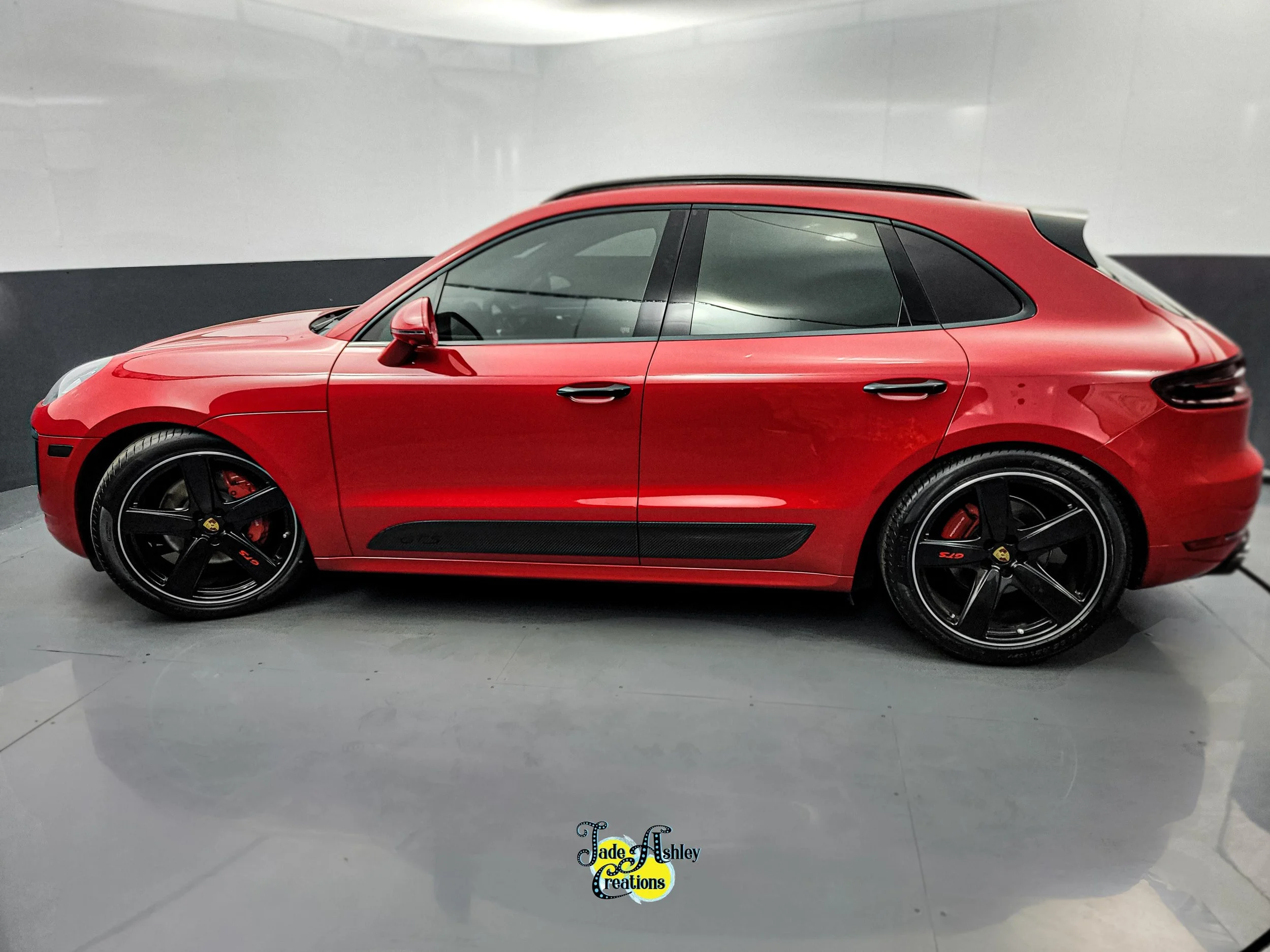 A red Porsche Macan parked indoors with black wheels, black accents, and a sleek design.
