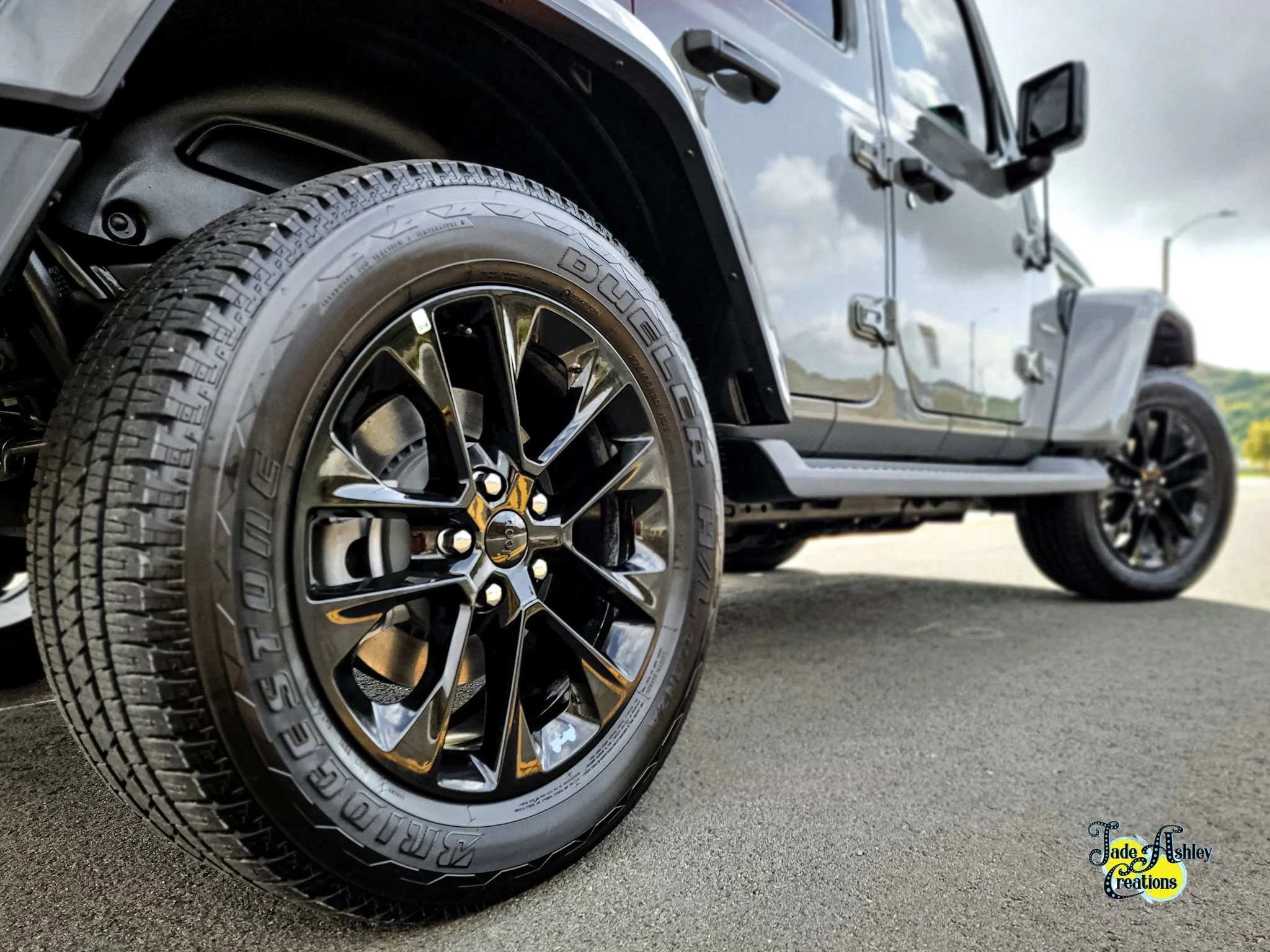 Close-up of a black SUV tire and rim, with a partial view of the vehicle body and side mirror.