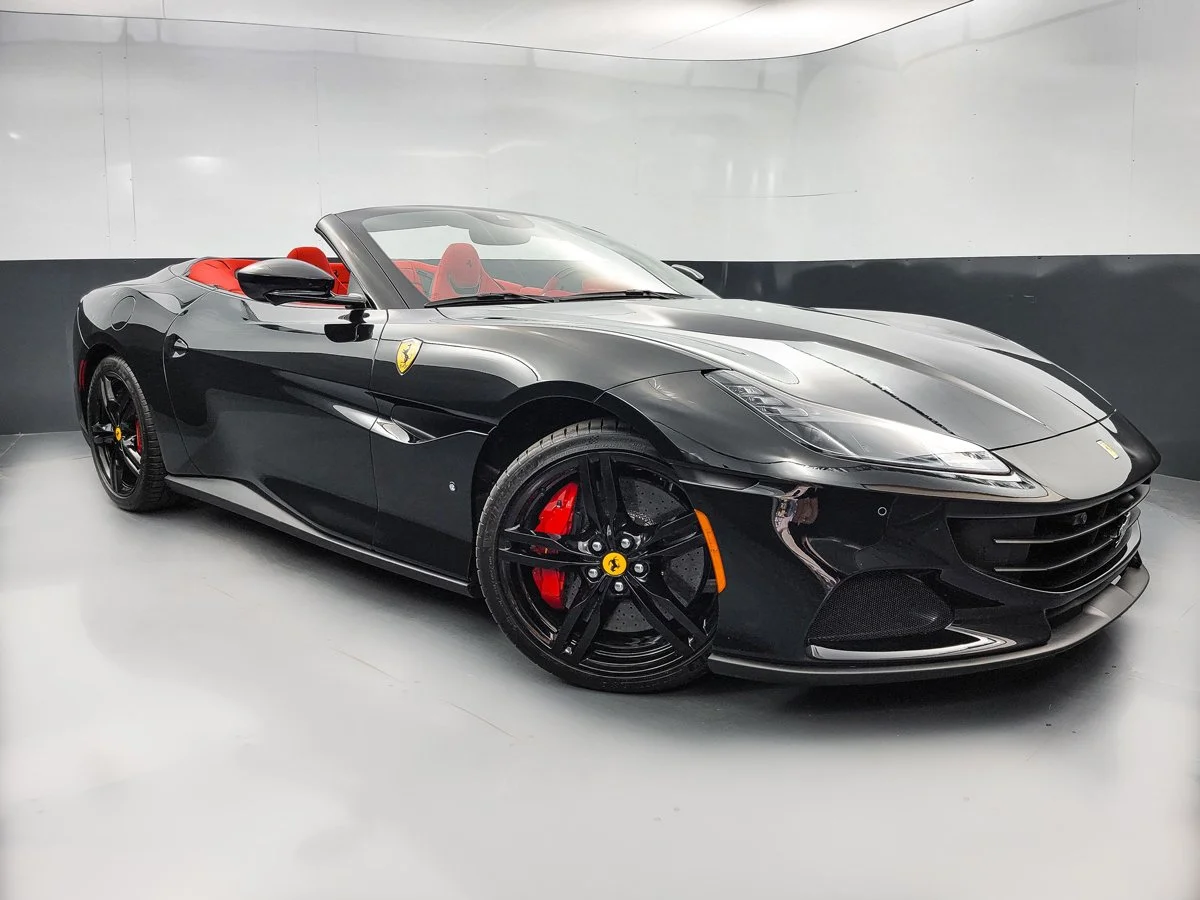 Black Ferrari convertible with red interior parked in an indoor showroom.