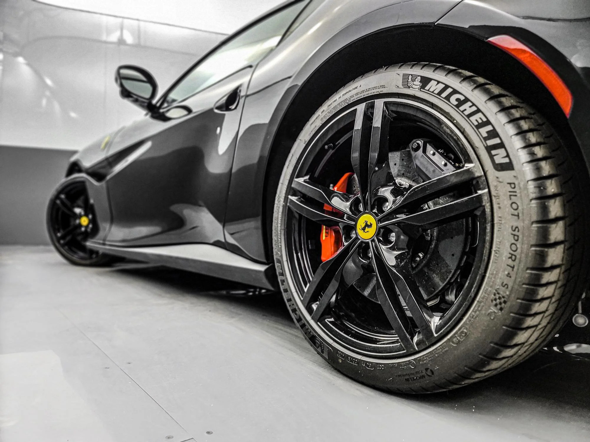 Close-up of a black Ferrari sports car showing the front wheel with Michelin Pilot Sport tires, black rims, and red brake calipers.