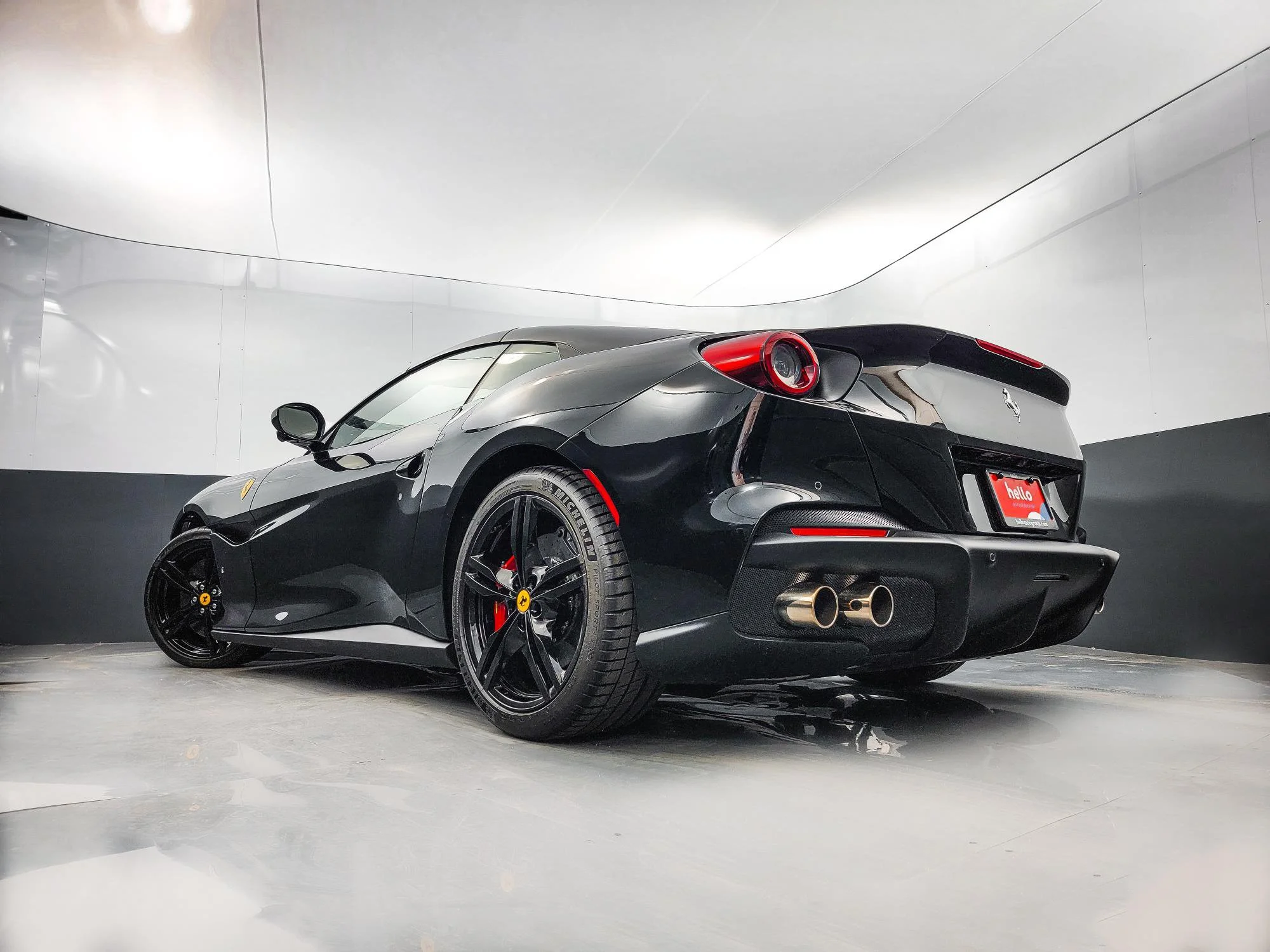 Black Ferrari sports car with two exhaust pipes in a modern indoor showroom.