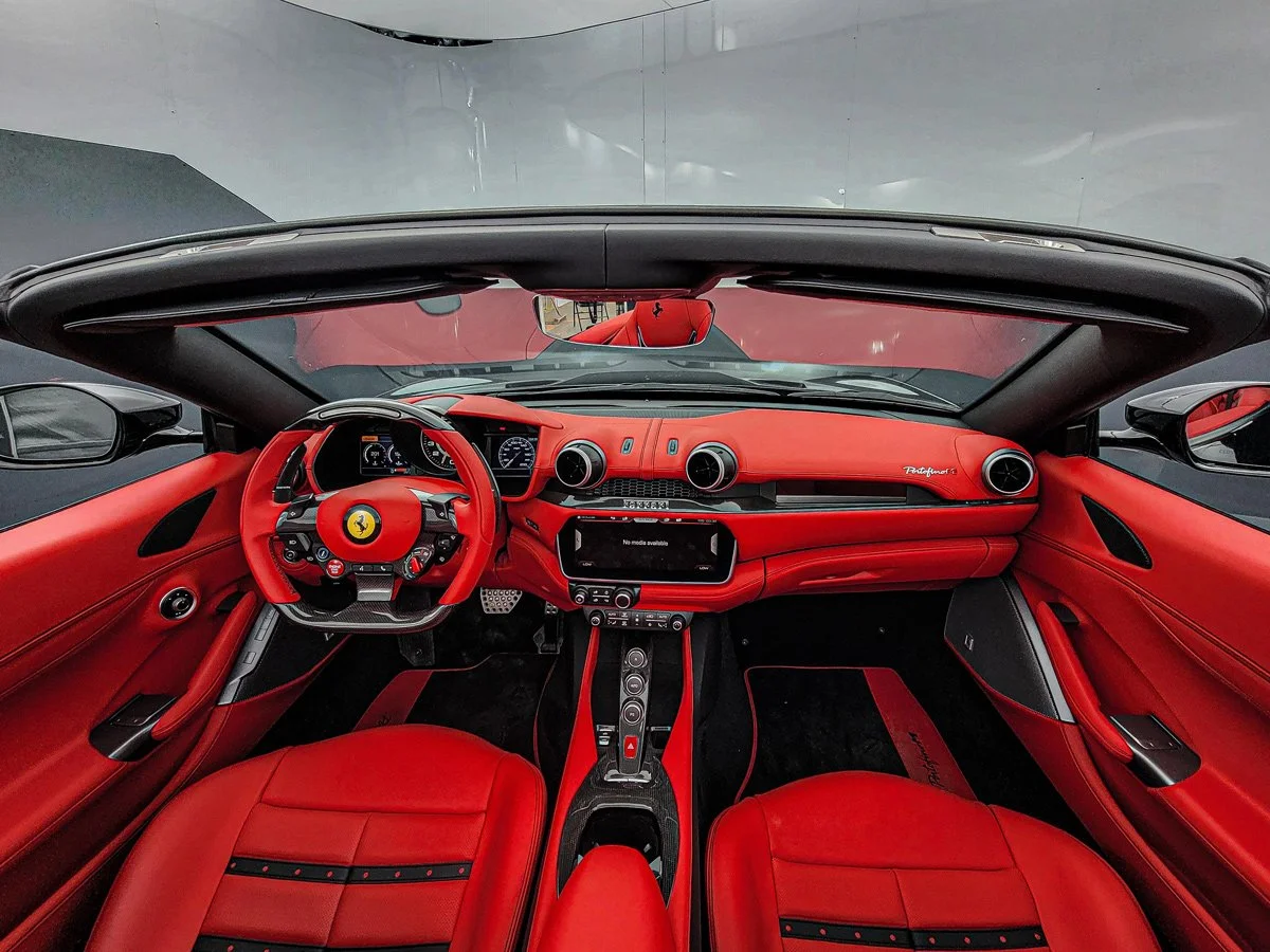 Interior of a red Ferrari convertible sports car showing the dashboard, steering wheel, and red leather seats.