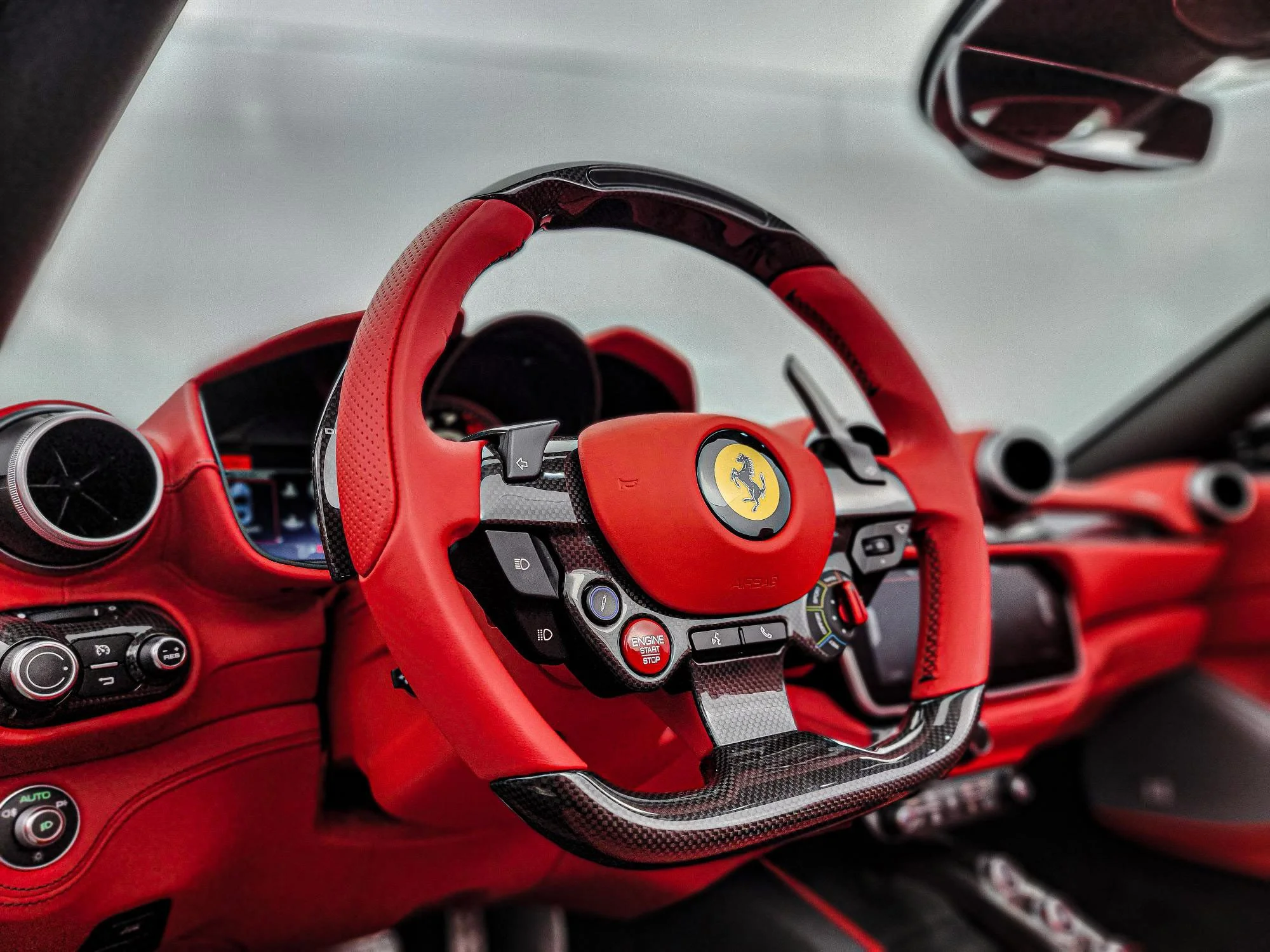 Inside view of a red Ferrari sports car, featuring a detailed dashboard and a steering wheel with the Ferrari logo, accented with black carbon fiber.