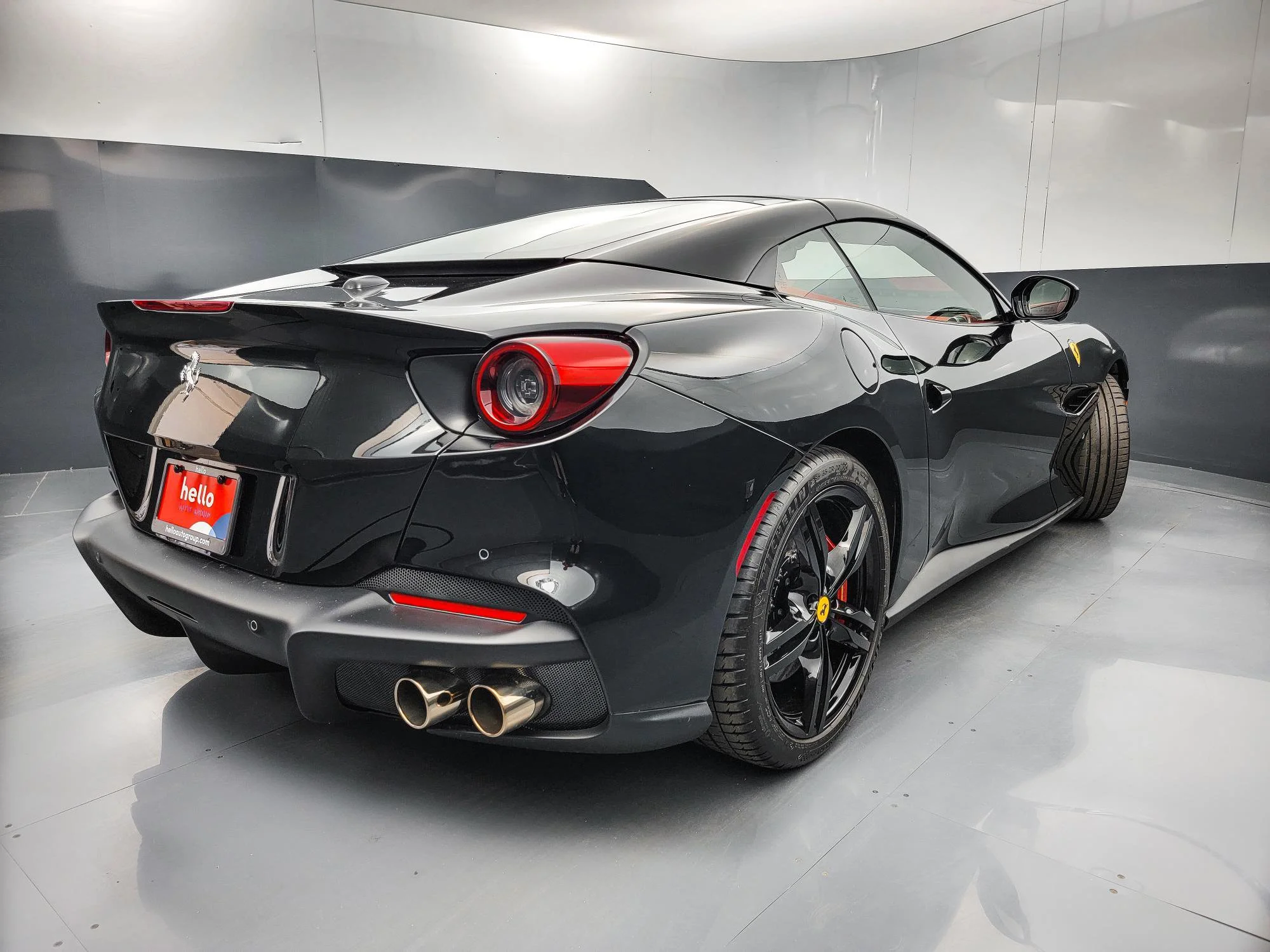 A black Ferrari sports car with red brake calipers, dual exhaust pipes, and a sleek aerodynamic design, parked indoors on gray flooring.