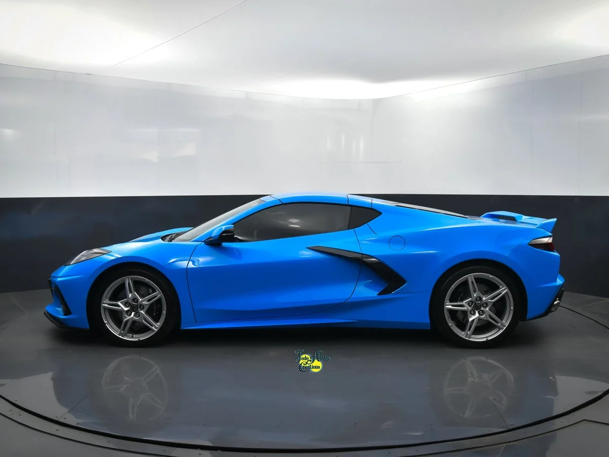 Blue sports car on display in a showroom with plain white and black walls.