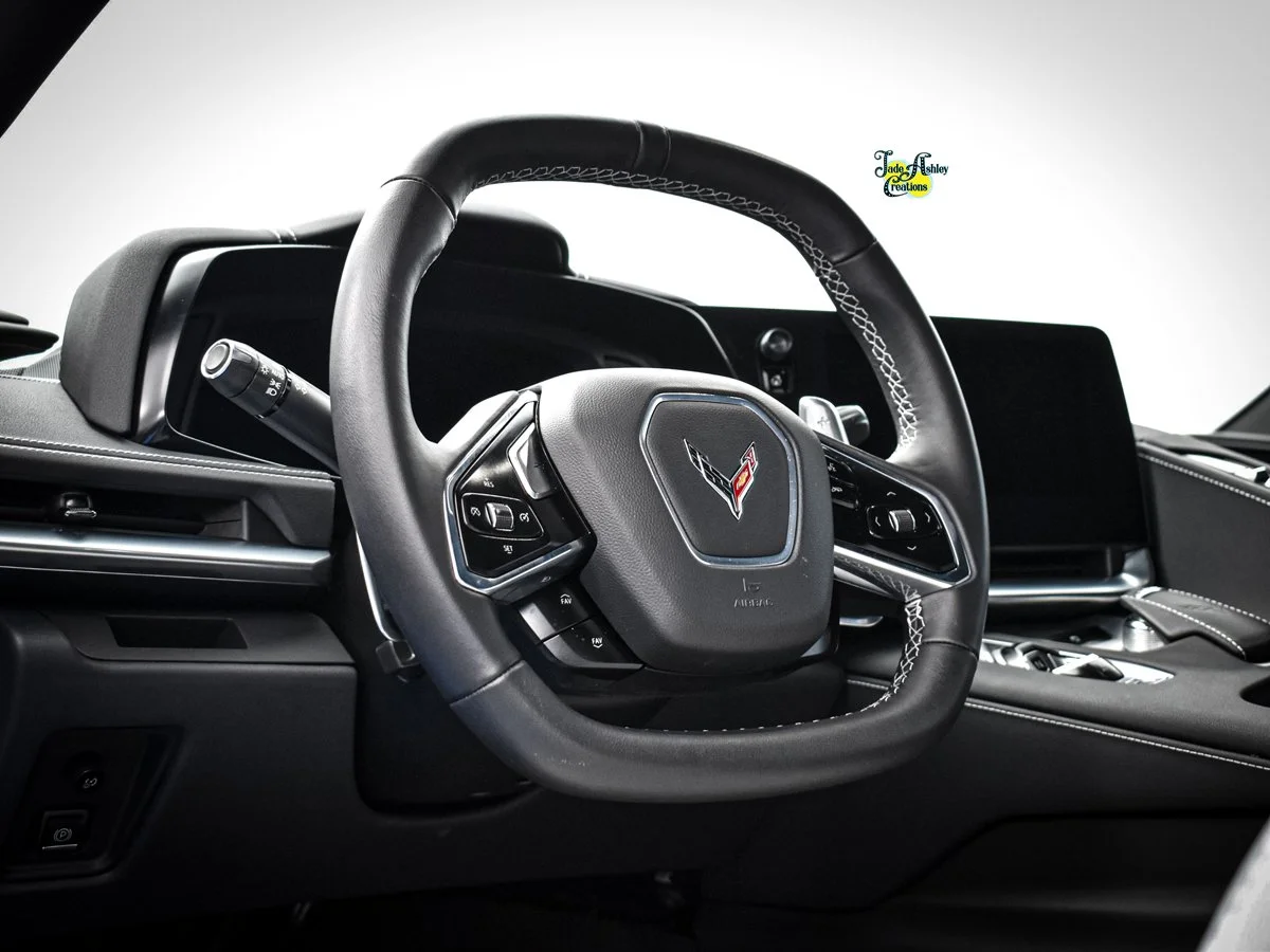 The interior of a car's dashboard featuring a steering wheel with the Chevrolet Corvette emblem in the center, digital display screens, and various control buttons.
