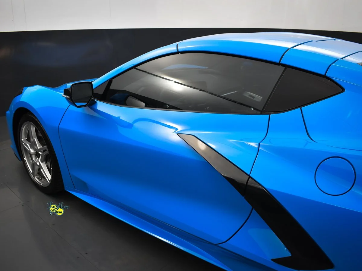 A sleek blue sports car with black accents, parked indoors on a black and gray surface, viewed from an elevated angle.